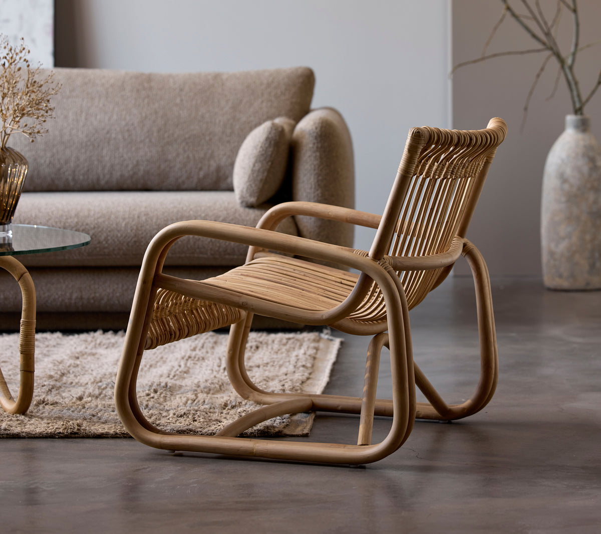 Rattanstol ved siden av en beige sofa og glassbord i et moderne loungeområde.