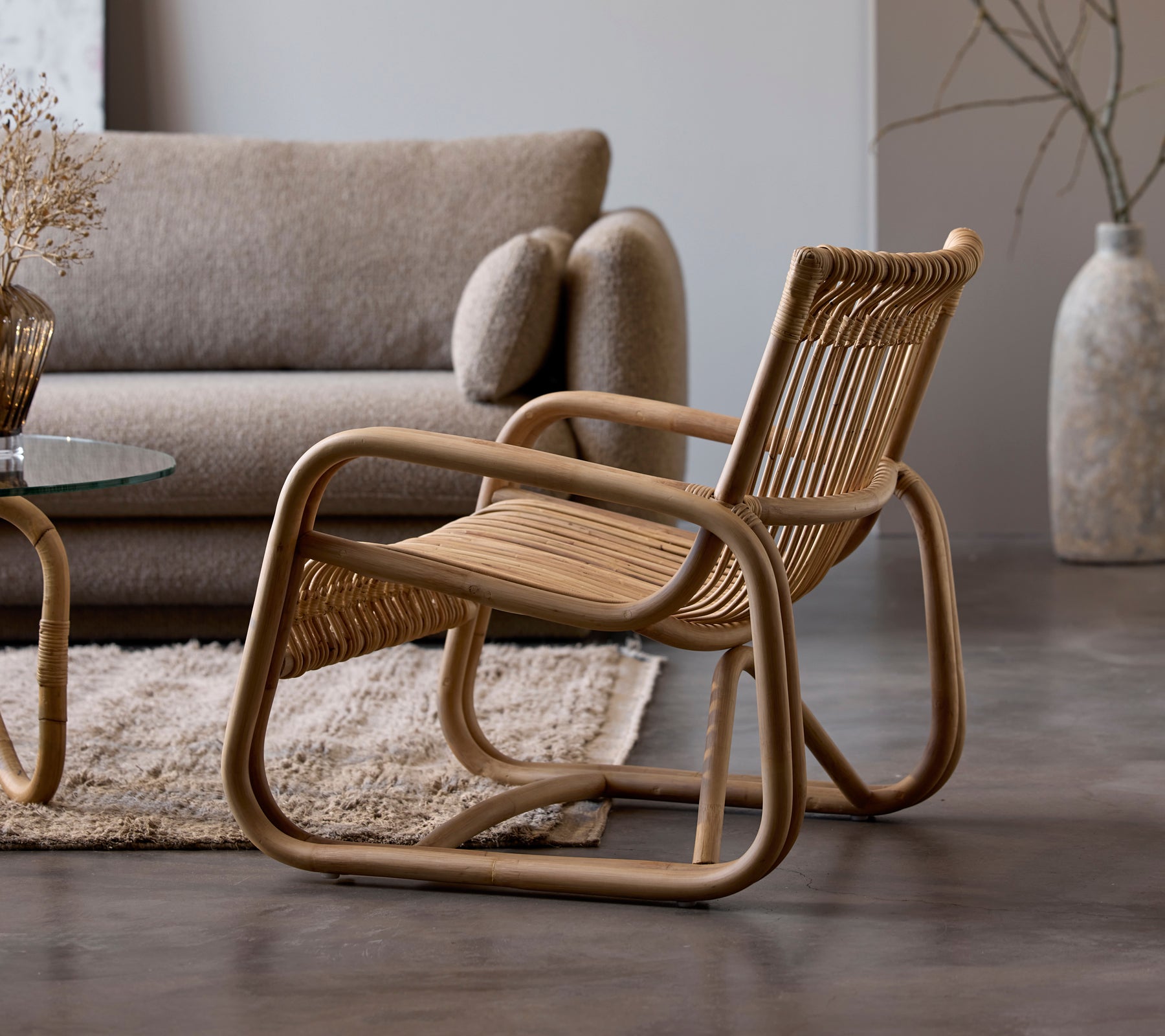 Rattanstol ved siden av en beige sofa og glassbord i et moderne loungeområde.