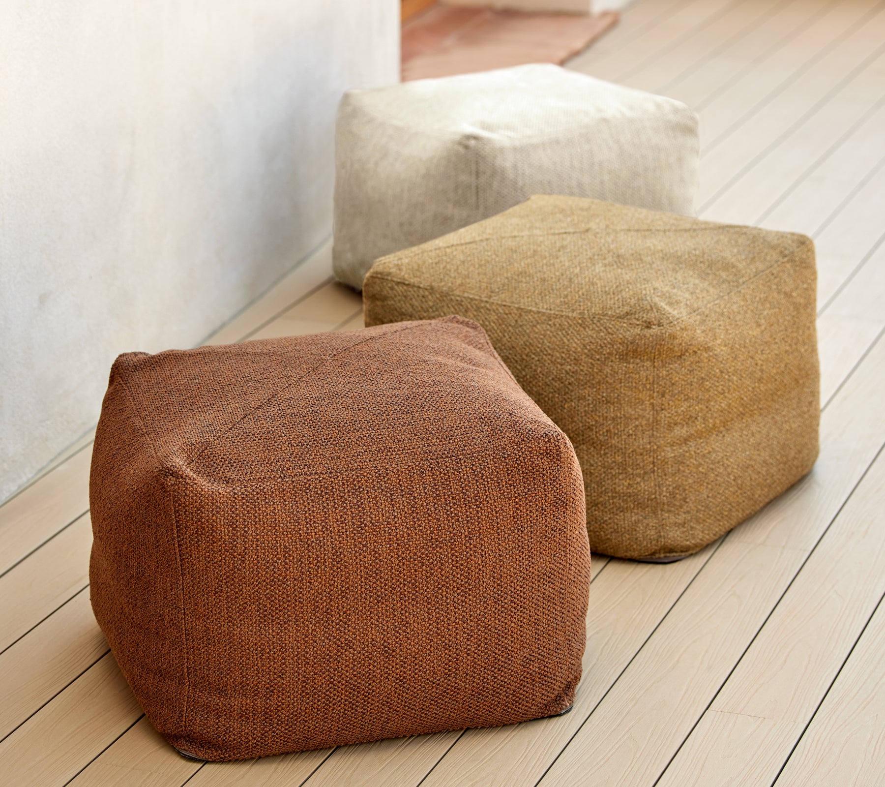 Tre teksturerte poufer i jordfarger som brunt, beige og tan, vist på en treoverflate. Ideelle for variert sitteplasser og dekor.