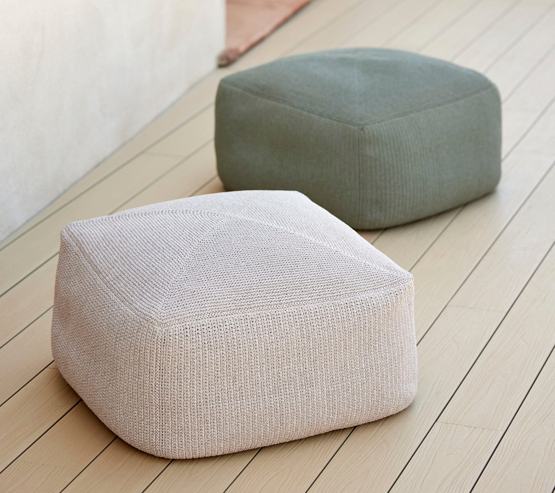 To stilige, teksturerte puffer i nøytrale toner, en hvit og en grønn, arrangert på en jevn overflate, ideell for allsidig seating.
