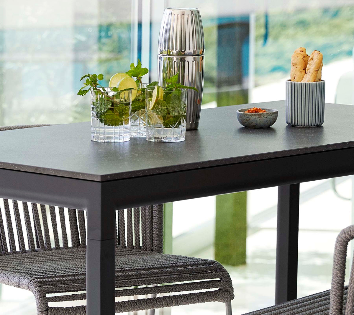 Et moderne bord satt med planter i glassvaser, en dekorativ beholder og en skål med snacks, omgitt av stilige stoler.