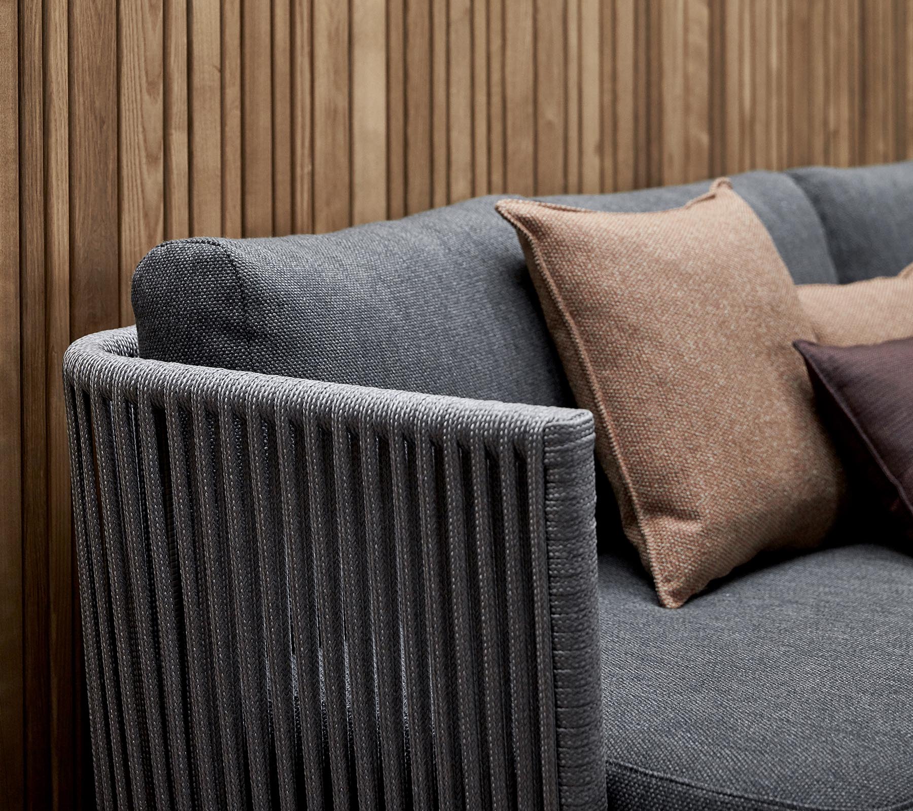 Stilig sofa med teksturert grått stoff og dekorative puter i jordfarger, samt en loddrett stripet armlene-design.