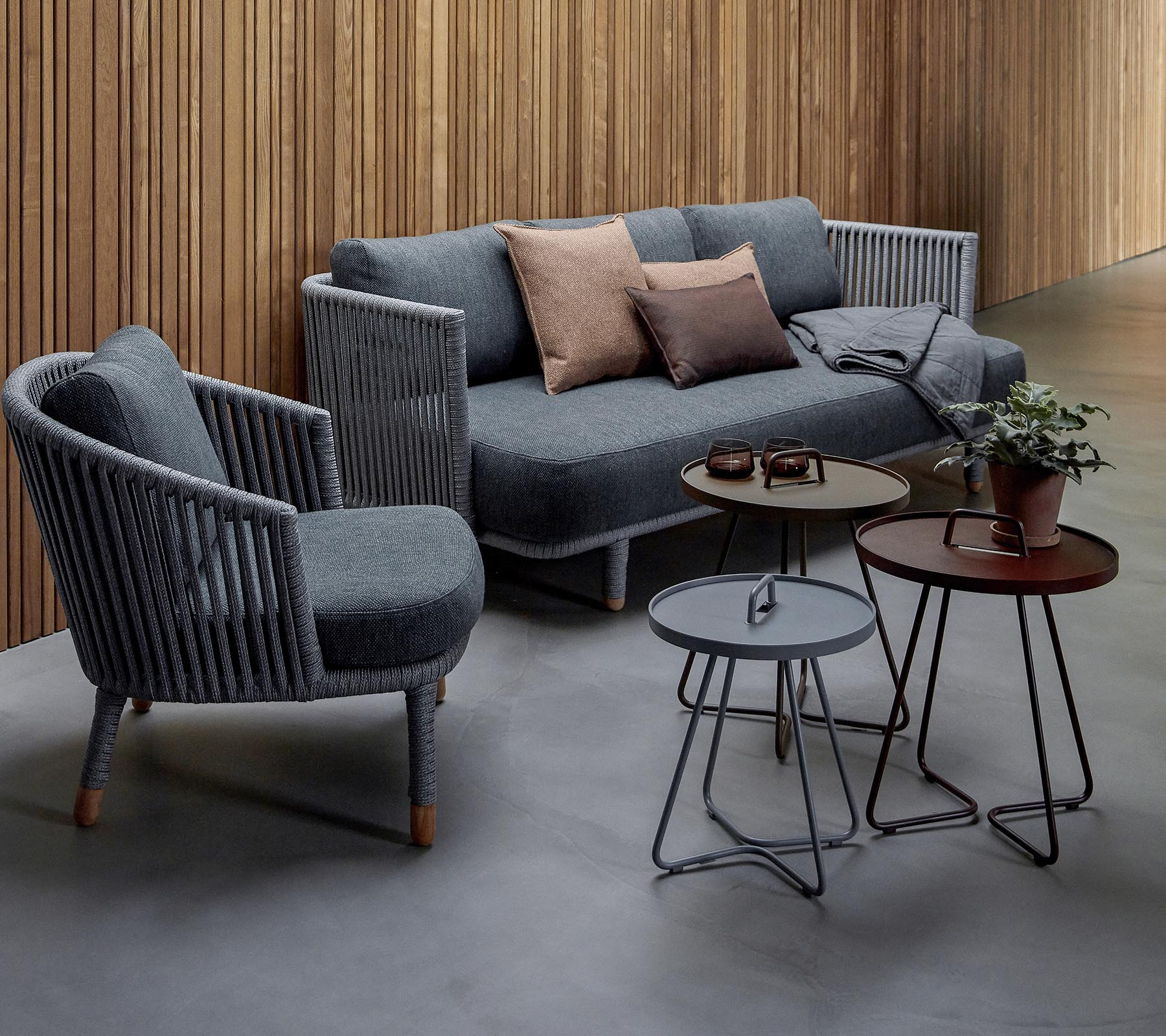 Stilig sittearrangement med en grå sofa med puter og to accentstoler, ledsaget av tre moderne bord og en potteplante.