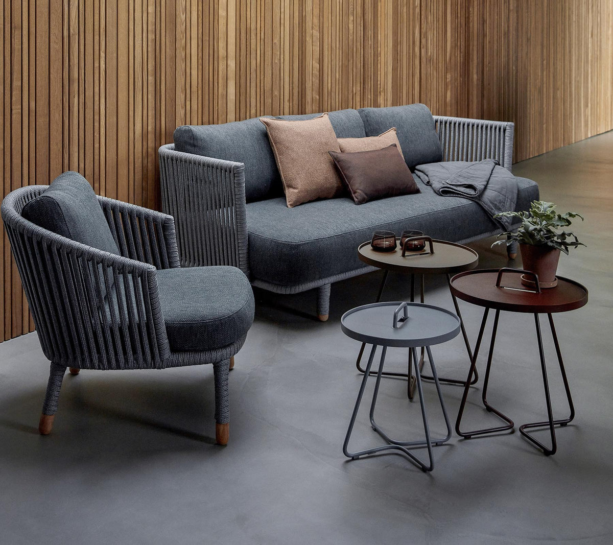 Stilig sittearrangement med en grå sofa med puter og to accentstoler, ledsaget av tre moderne bord og en potteplante.