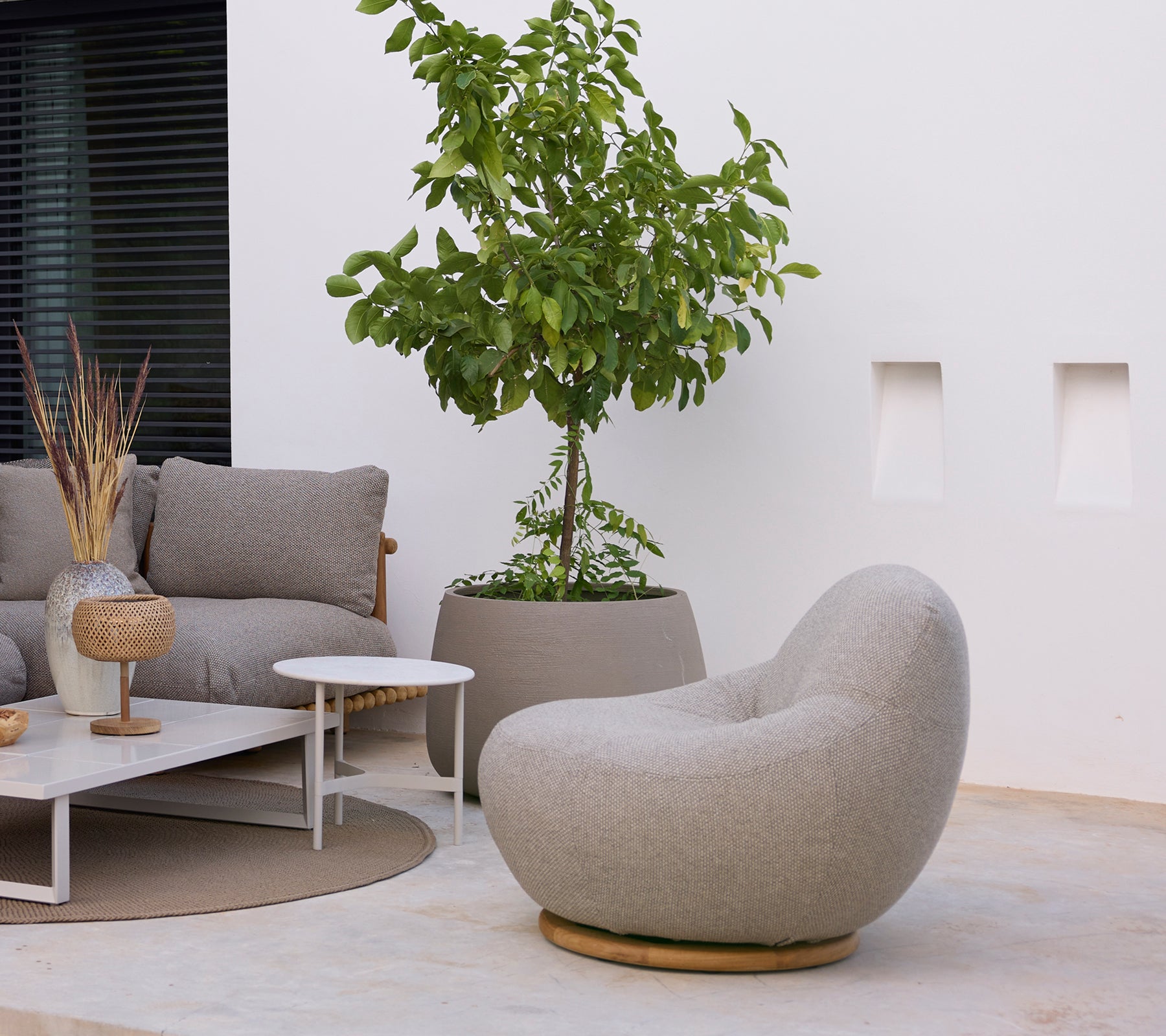 Moderne loungeområde med en grå stol, sofa, hvitt salongbord og grønn plante.