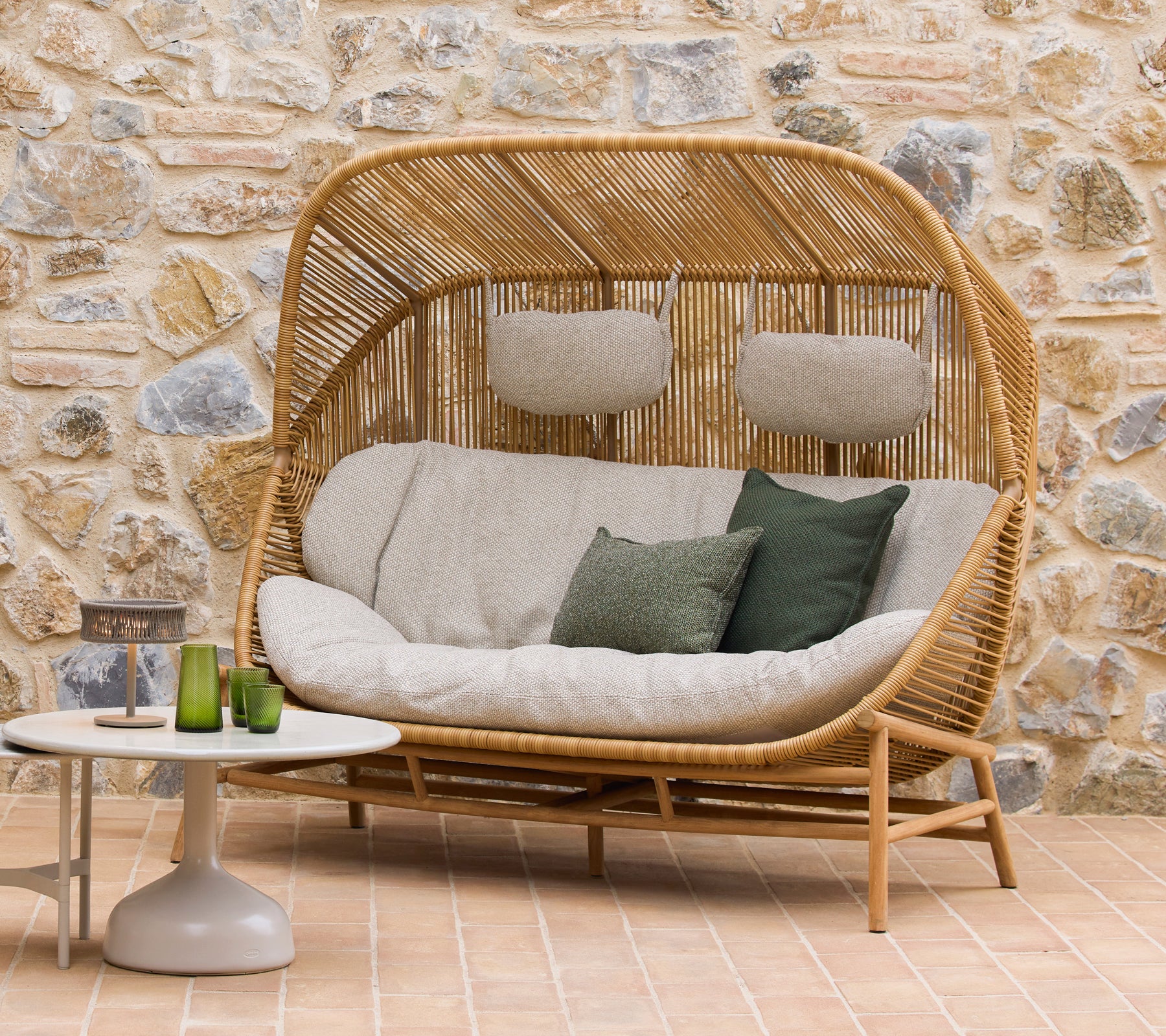 Hive-sofa med myke puter og grønne accenter sammen med Glaze-kaffebord, satt mot en naturlig steinbakgrunn.