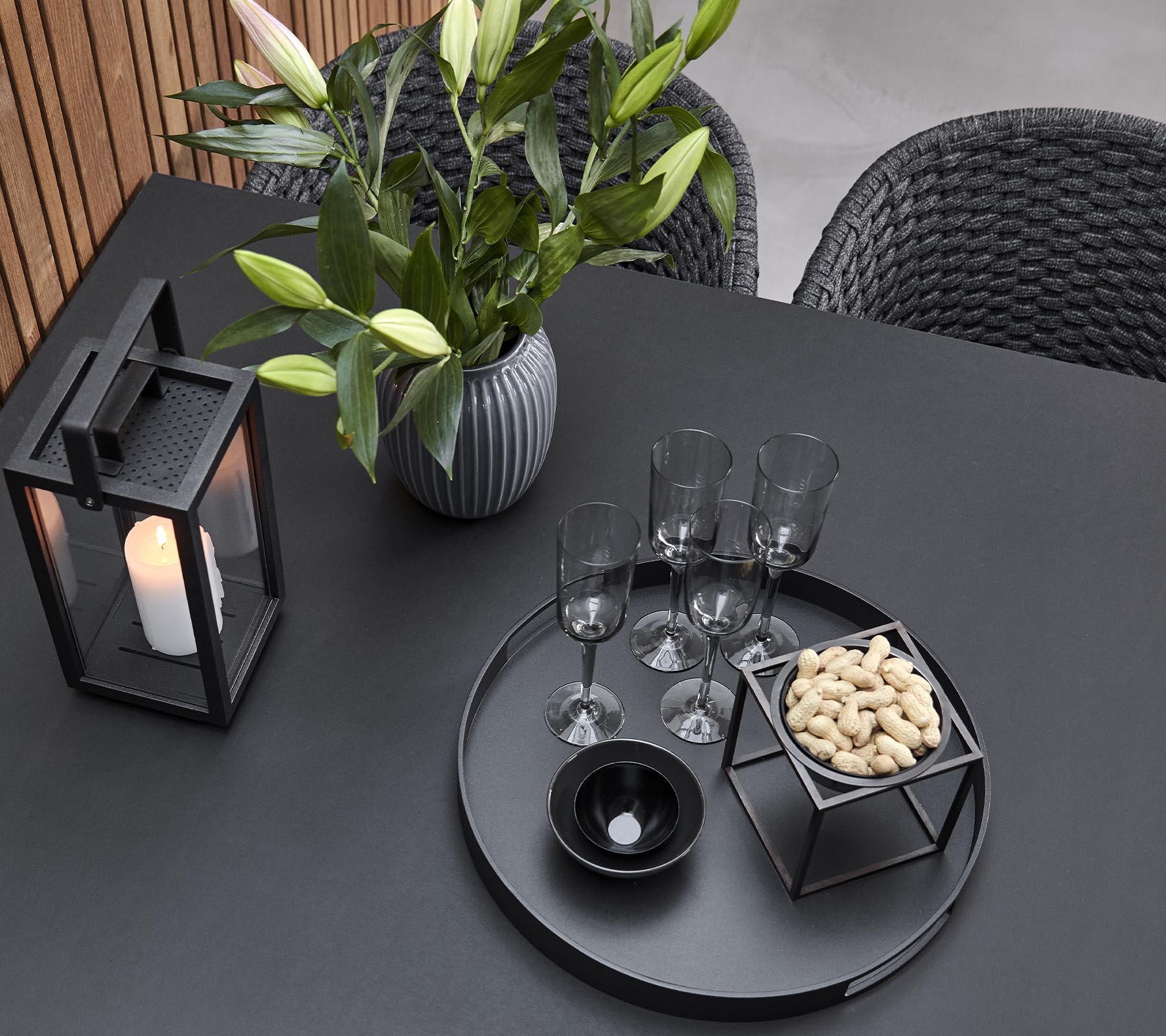 Et stilfullt bordoppsett med en lykt, en vase med blomster, glass og et serveringsbrett med snacks.