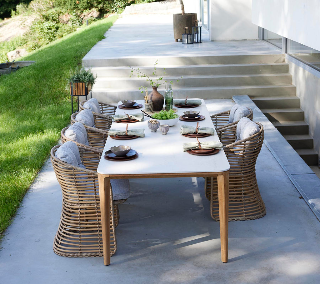 Et stilrent ute spisestuebordsett med runde kurvstoler, elegant dekorert med tallerkener og et midtpunkt av grønne planter.