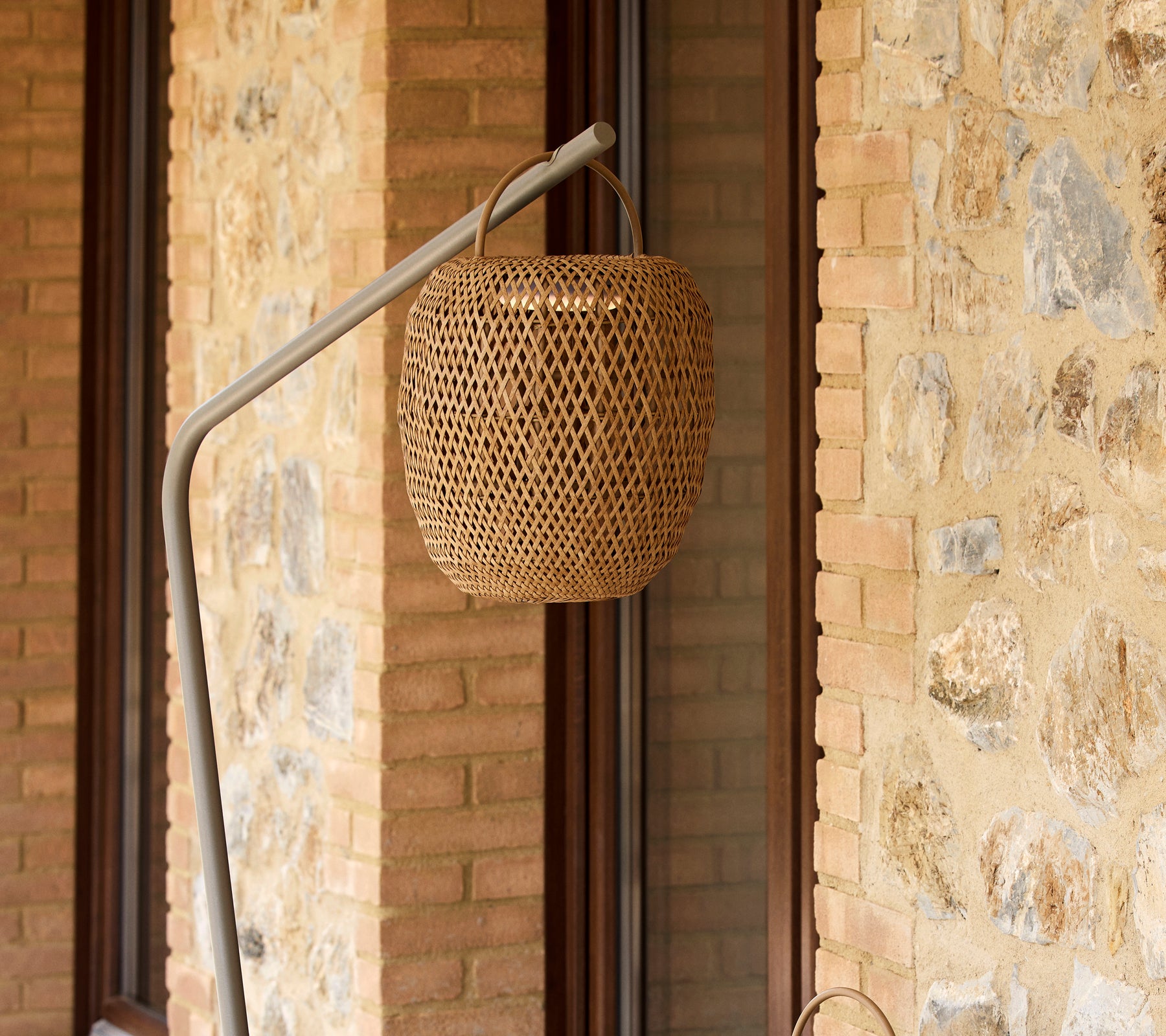 En vevd, lysende lampe hengende fra et slankt stativ, som komplementerer en teksturert steinvegg.