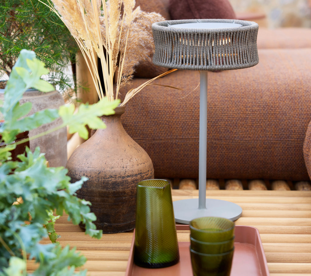 En medium illusjonslampe på toppen av et klubbfat, omgitt av grønne glass og dekorative planter.
