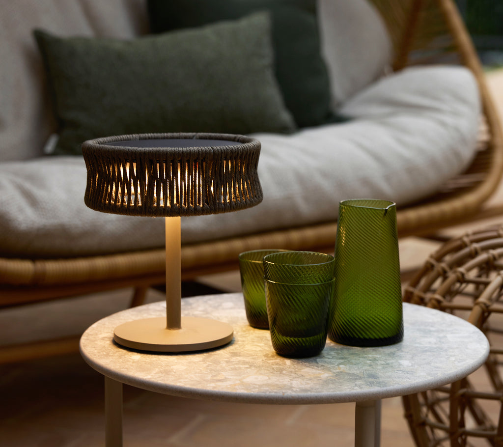 En liten mørkegrå illusjonslampe på et marmor kaffebord, akkompagnert av grønne dekorative glassvaser og et koselig sitteområde.