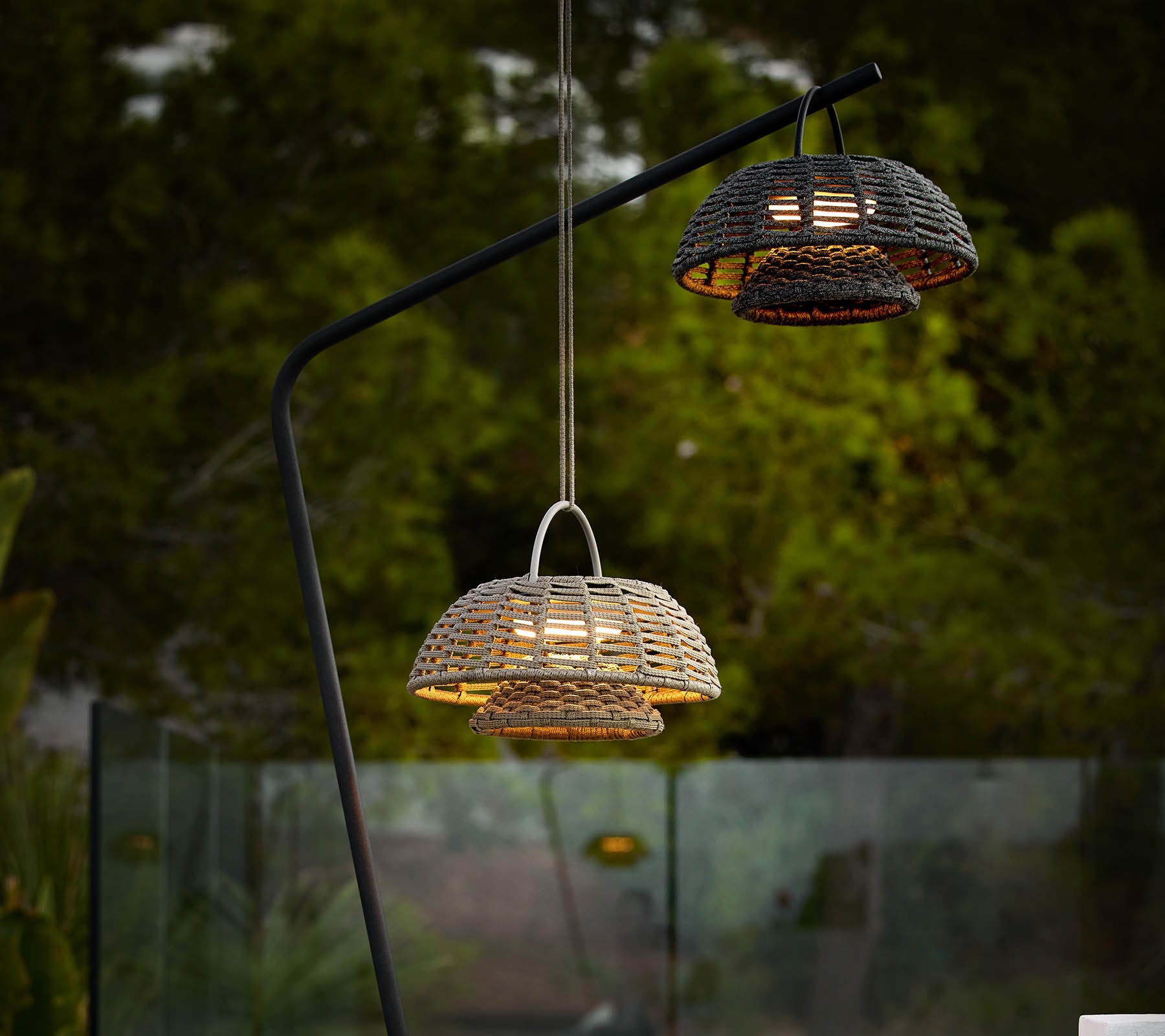 To illusjonslamper med vevde design, hengende fra en elegant svart stativ, som kaster varmt lys mot en mørk bakgrunn.