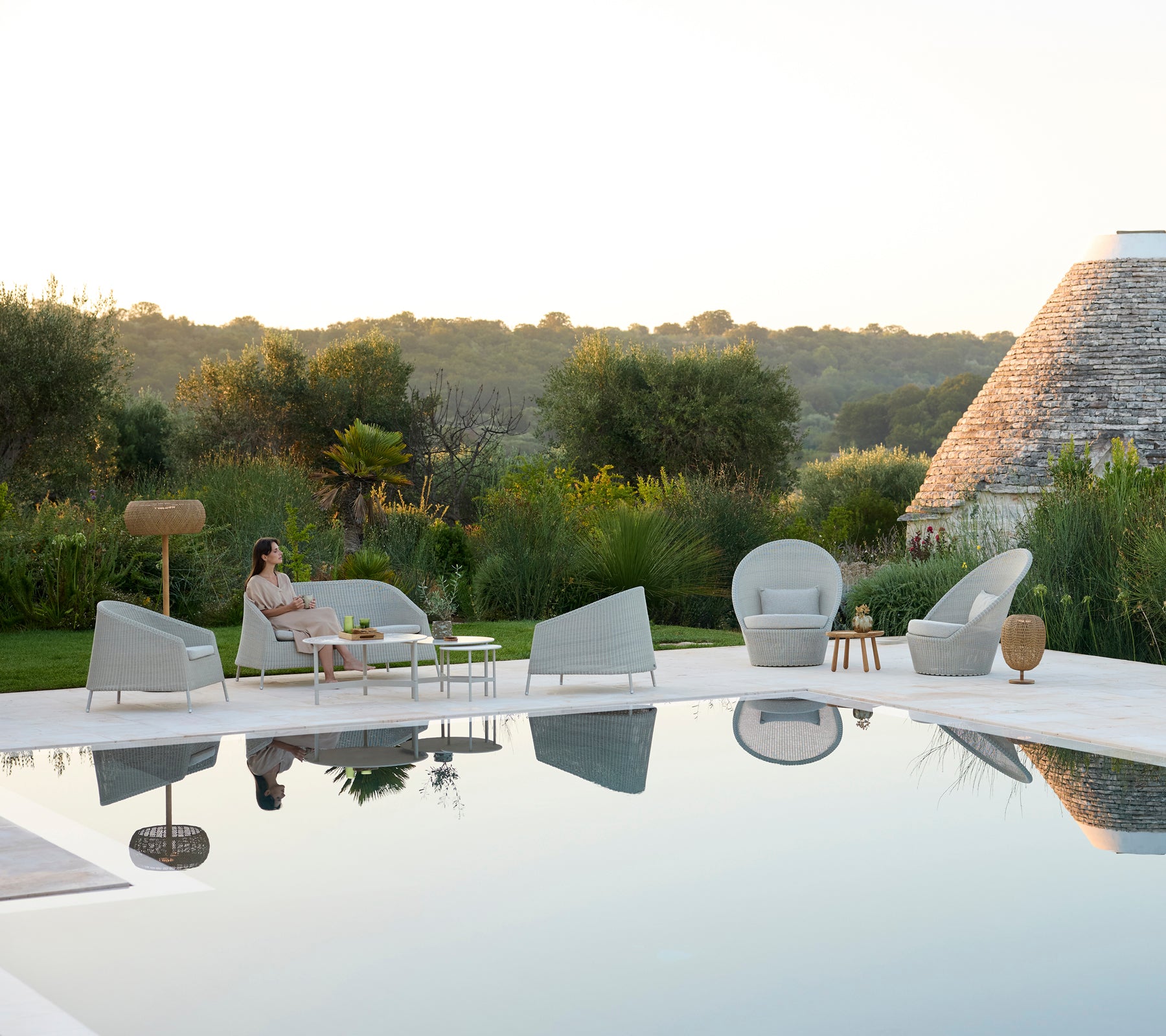 Moderne utendørs loungeområde med grå stoler og et hvitt bord ved et basseng.