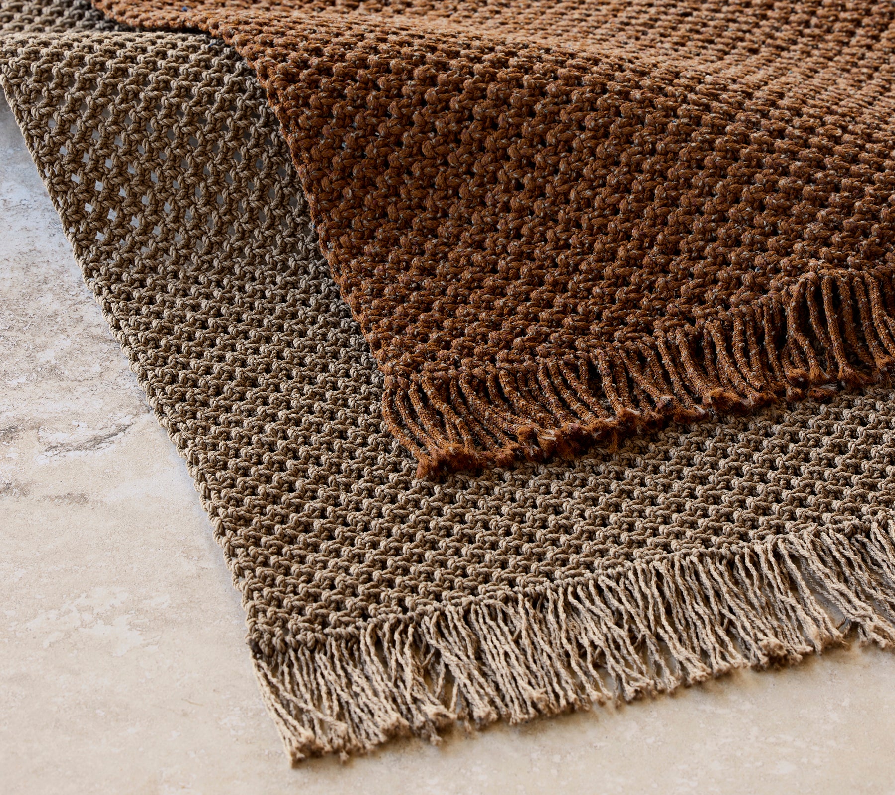Strikket teppe som måler 240x170 cm i et strukturert mønster med frynser, med varme brune toner.