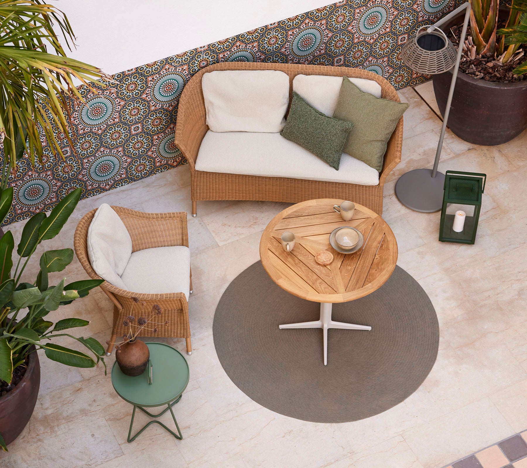 En koselig sittearrangement med en rattan-sofa, et rundt trebord og potteplanter, som forbedrer en stilfull atmosfære.