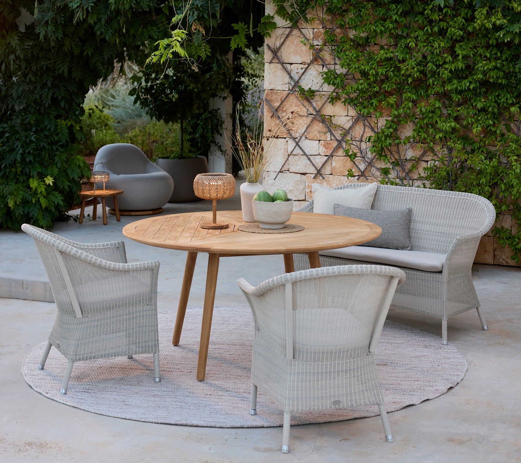 Moderne loungeområde med grå stoler, et rundt tresbord og en grå sofa omgitt av grønt.