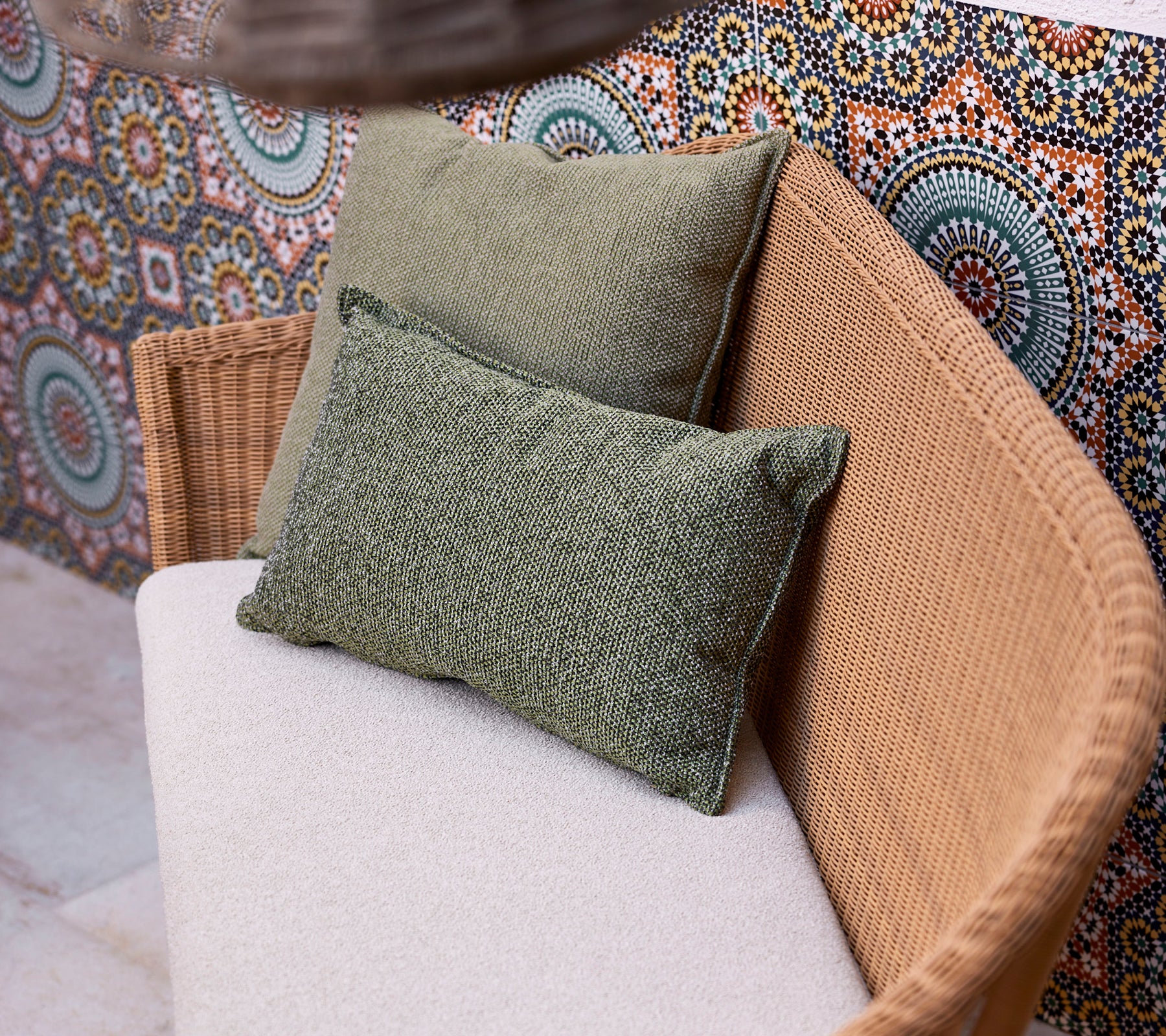 To grønne puter på en lys sofa, plassert mot en livlig, mønstret bakgrunn med sirkulære design.