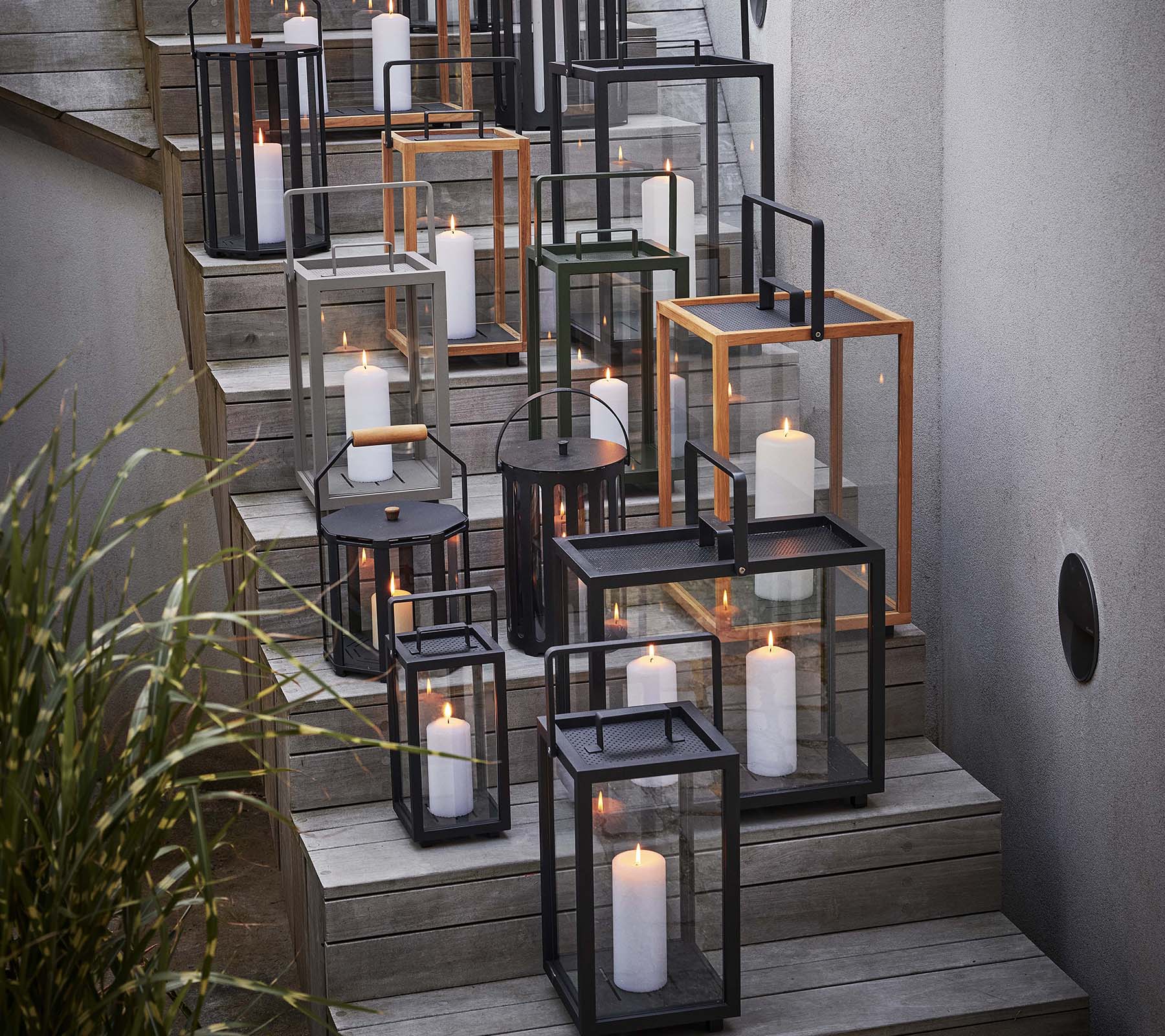 En samling av ulike lanterner med lys arrangert på en trapp, som viser en blanding av svarte og metalliske rammer.
