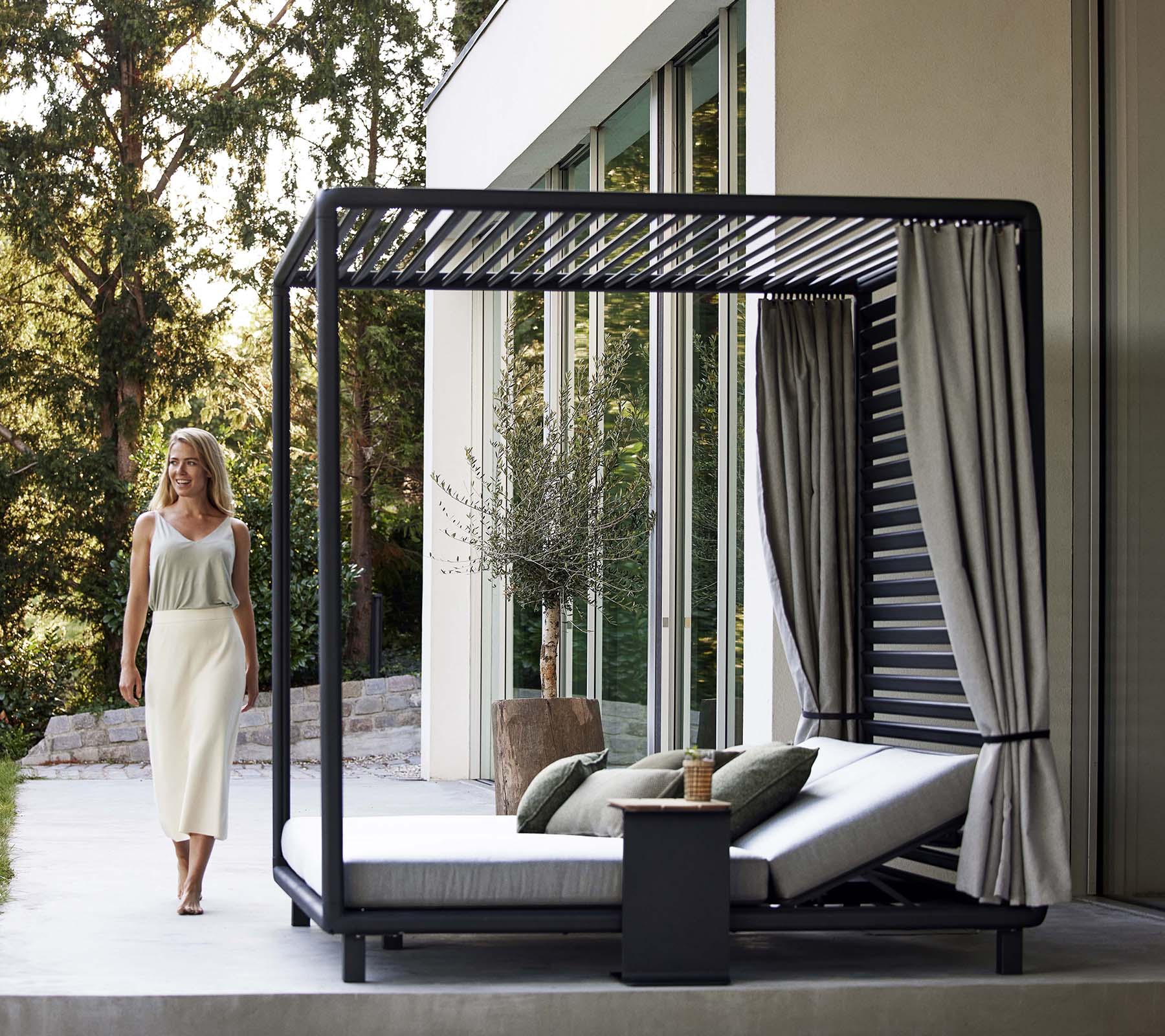 En stilig cabana med et elegant design, myke puter, gardiner og et lite sidebord, plassert i et rolig, naturlig miljø.