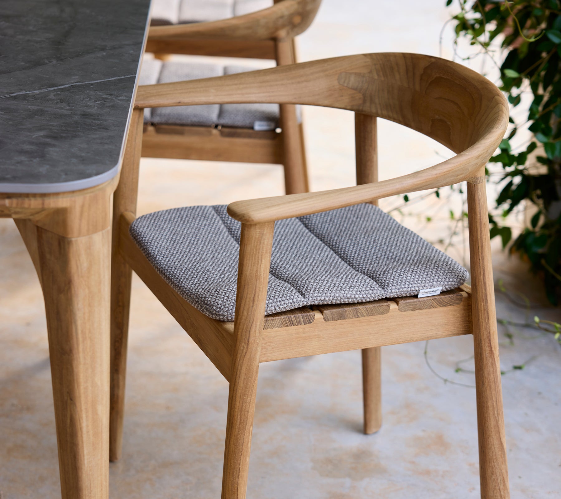 Moderne trebordstol med grå pute ved siden av et bord i en loungeinnstilling.