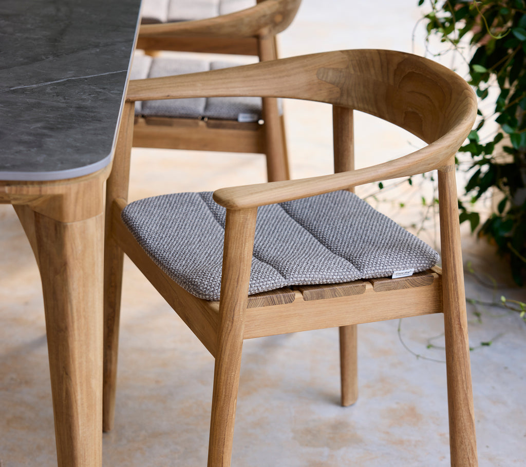 Moderne trebordstol med grå pute ved siden av et bord i en loungeinnstilling.