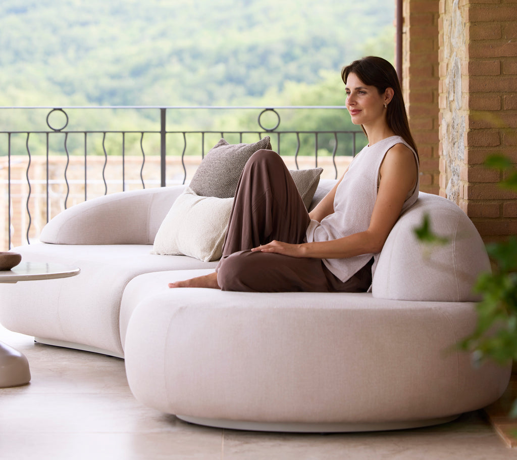 En kvinne sitter komfortabelt på en elegant, moderne sofa, akkompagnert av dekorative puter, og nyter en fredelig utsikt over naturen.