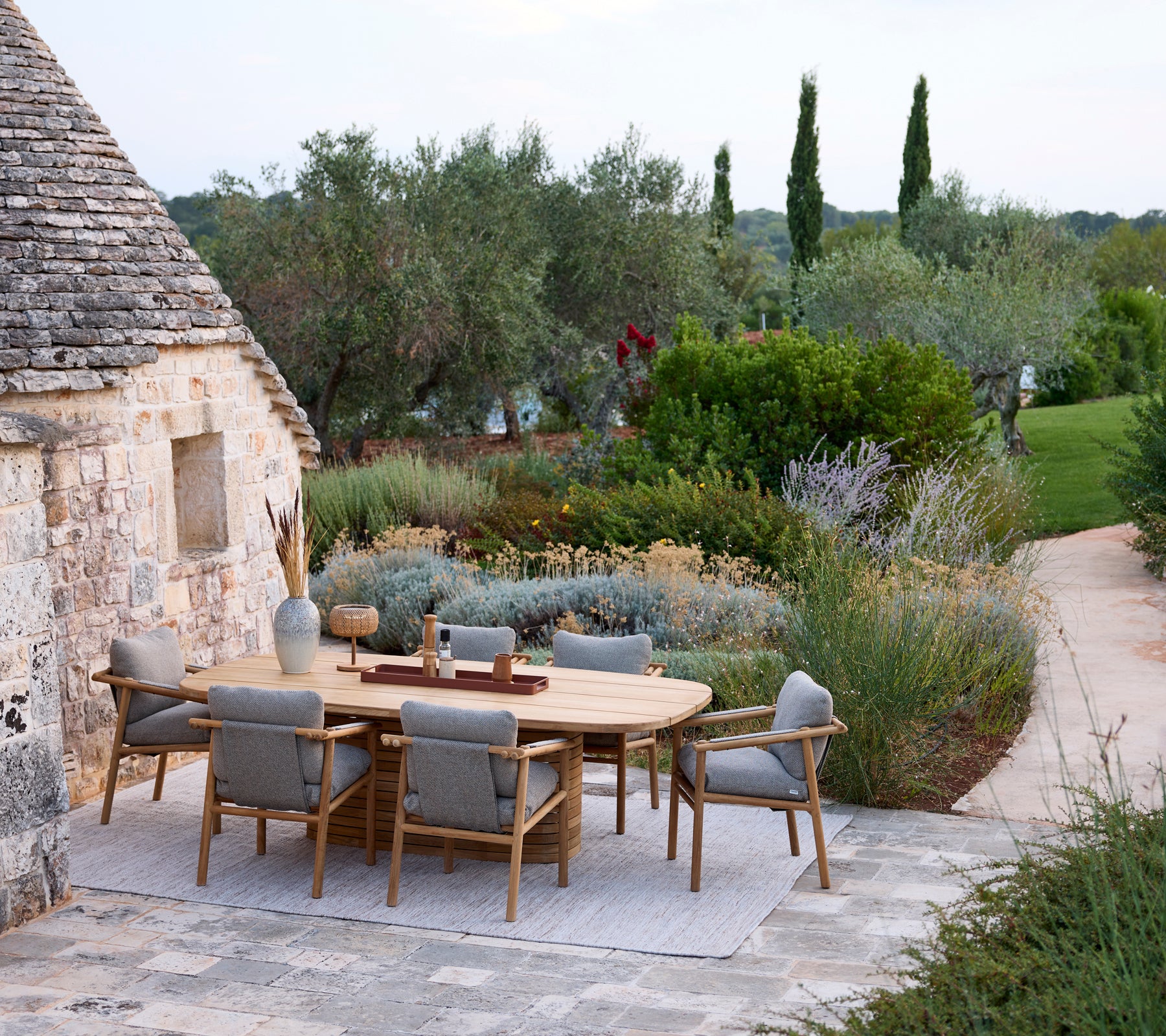 Moderne utendørs spisestue med rundt bord og grå stoler omgitt av grønt.