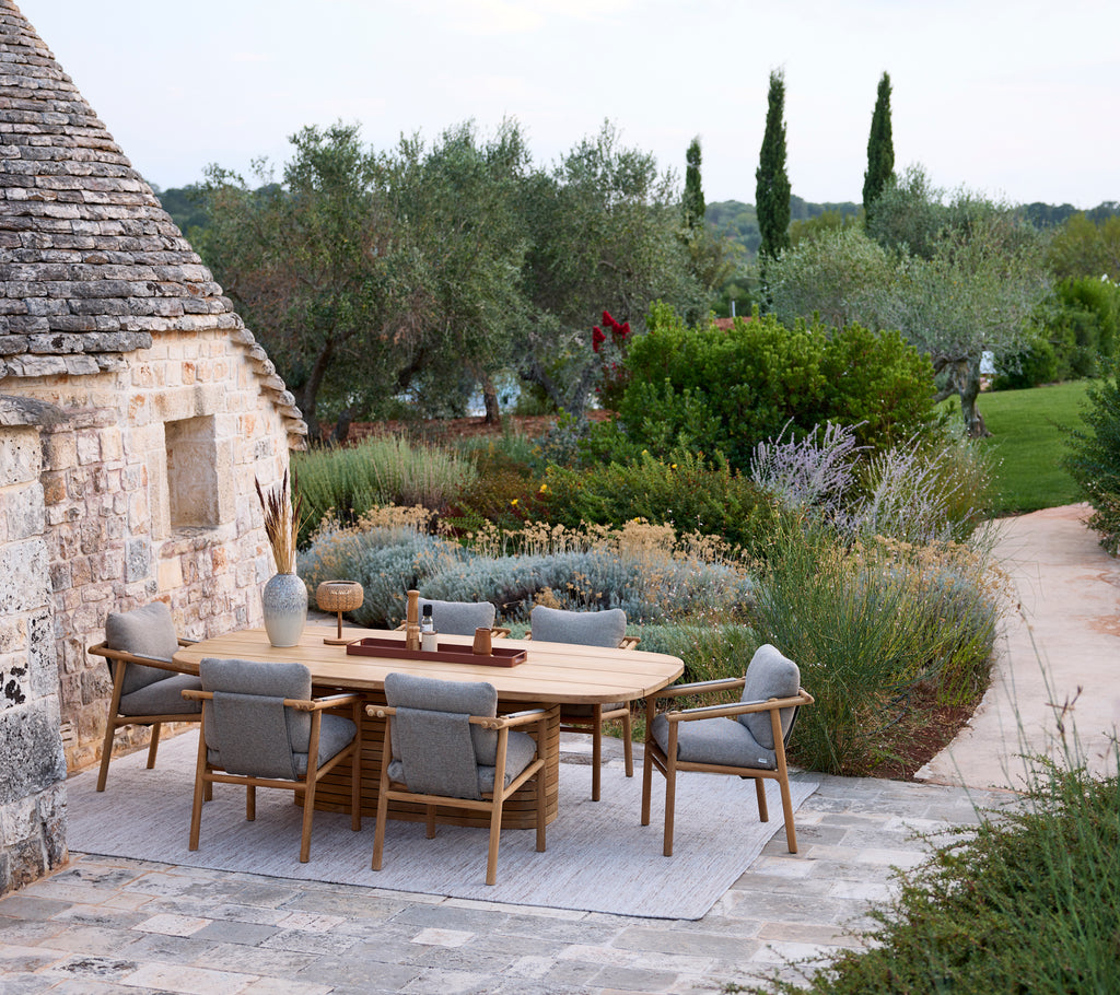 Moderne utendørs spisestue med rundt bord og grå stoler omgitt av grønt.