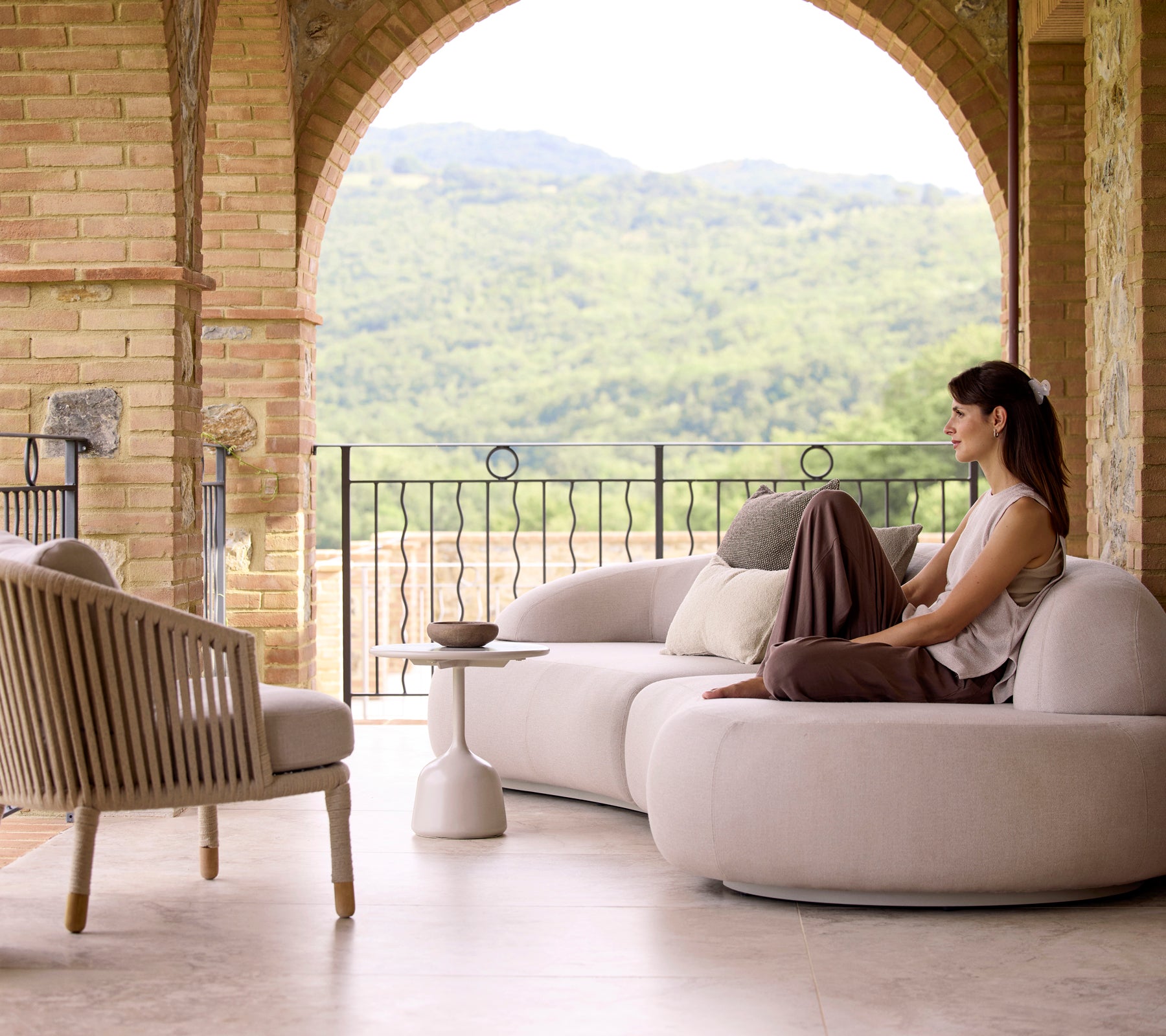Et stille sitteområde med en myk loungesofa, en Moments-lounge stol og et Glaze kaffebord, med frodig grønt bakgrunn.