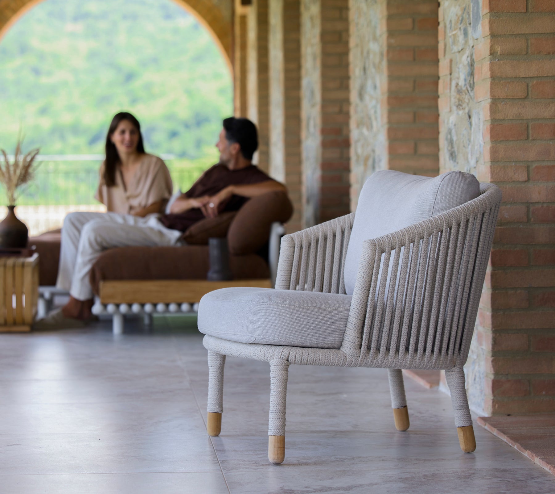 En sandfarget loungestol med minimalistisk design, vist i en rolig setting med folk som er engasjert i samtale.
