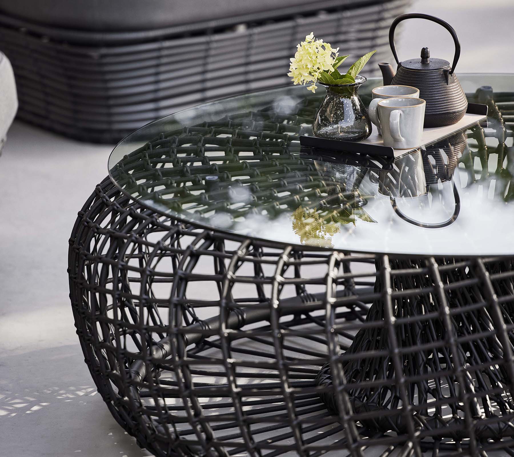 Nest kaffebord med vevd base, en glassplate og et tesett med blomster for et stilfullt, moderne utseende.