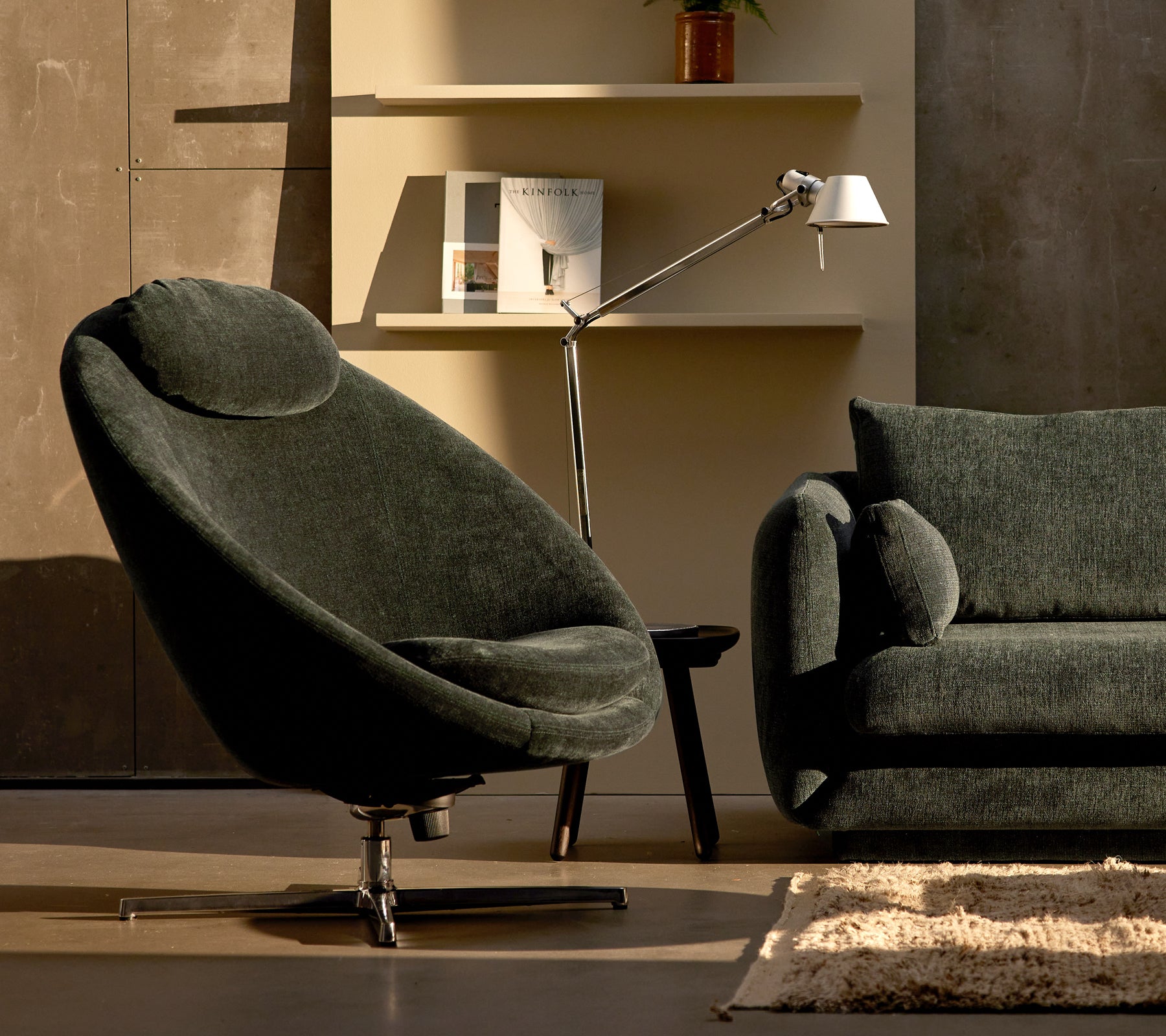 Pace-stol i mørkegrønn chenille ved siden av en Bloom-sofa, komplementert av en slank lampe og minimalistisk hyldedekor.