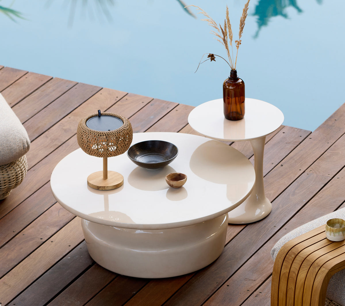 Moderne utendørsinnredning med hvite kaffe- og sidebord, gulllysholder og brun vase.
