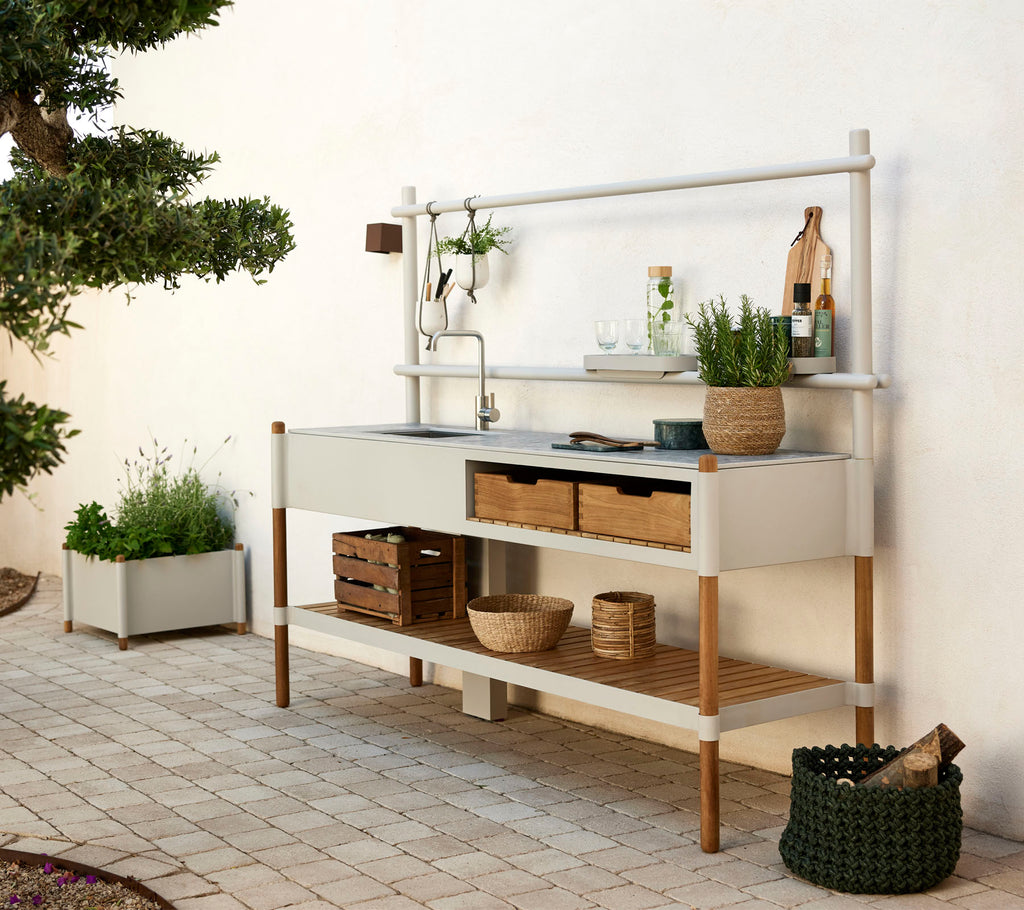 Moderne kjøkkenenhet med en metallvask, tregyller og dekorative planter i stilige beholdere. Rent design med naturlige elementer.
