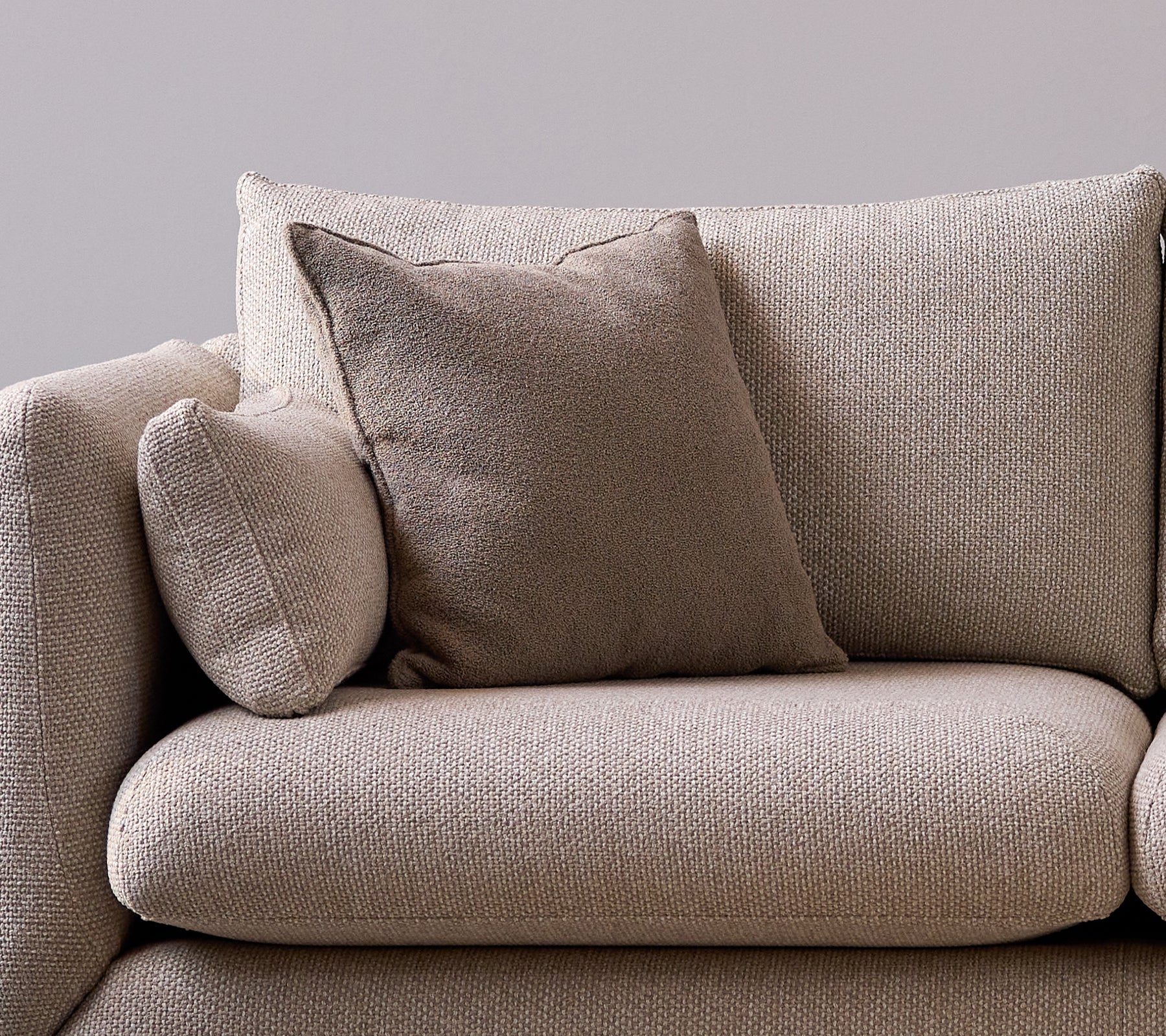 Taupe duftscatterpute på en myk, teksturert sofa som gir en koselig og stilfull touch til sitteområdet.
