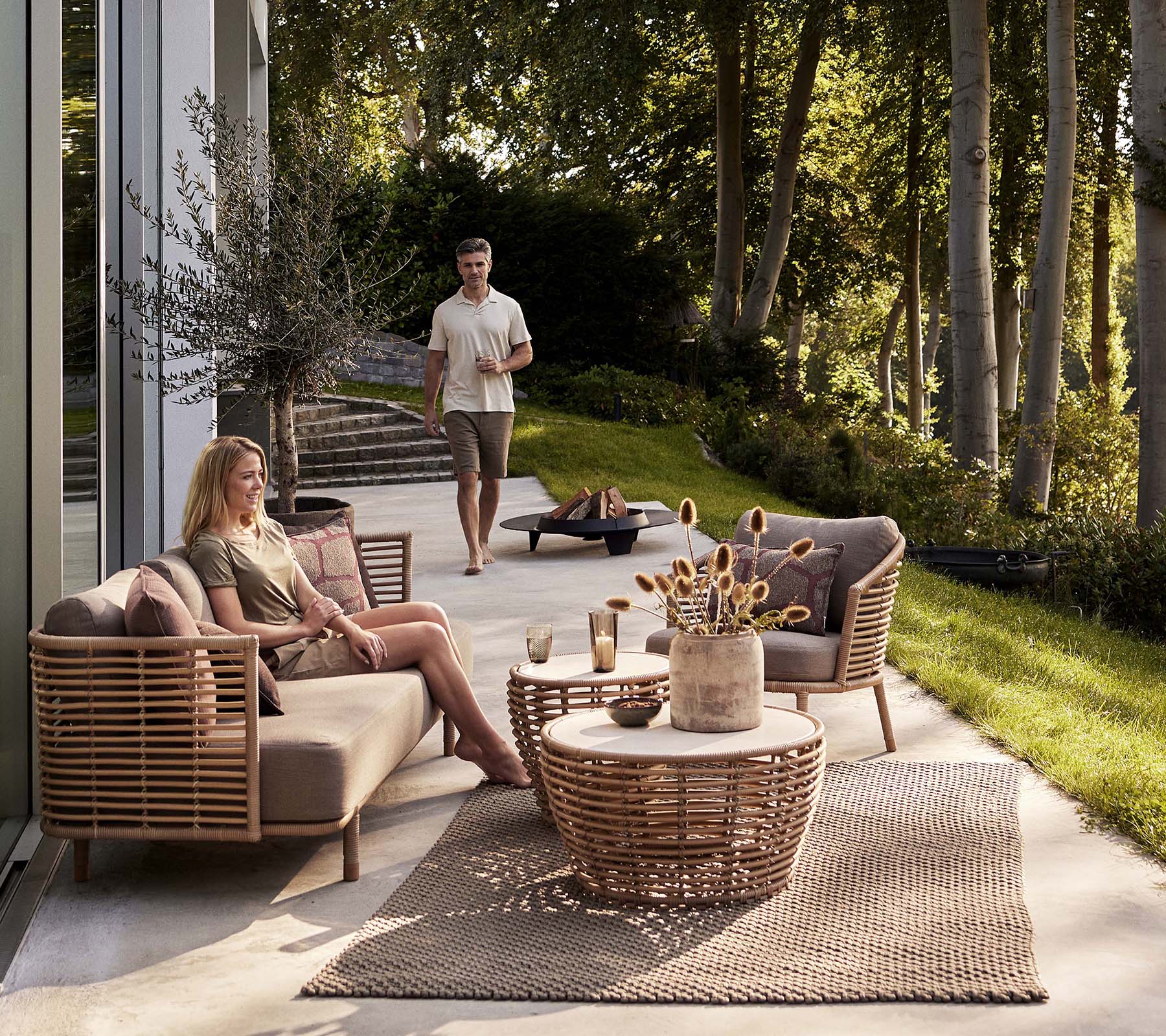 Et koselig sittearrangement med en Sense-sofa og en loungestol, akkompagnert av et kurvkaffebord og dekorative elementer.