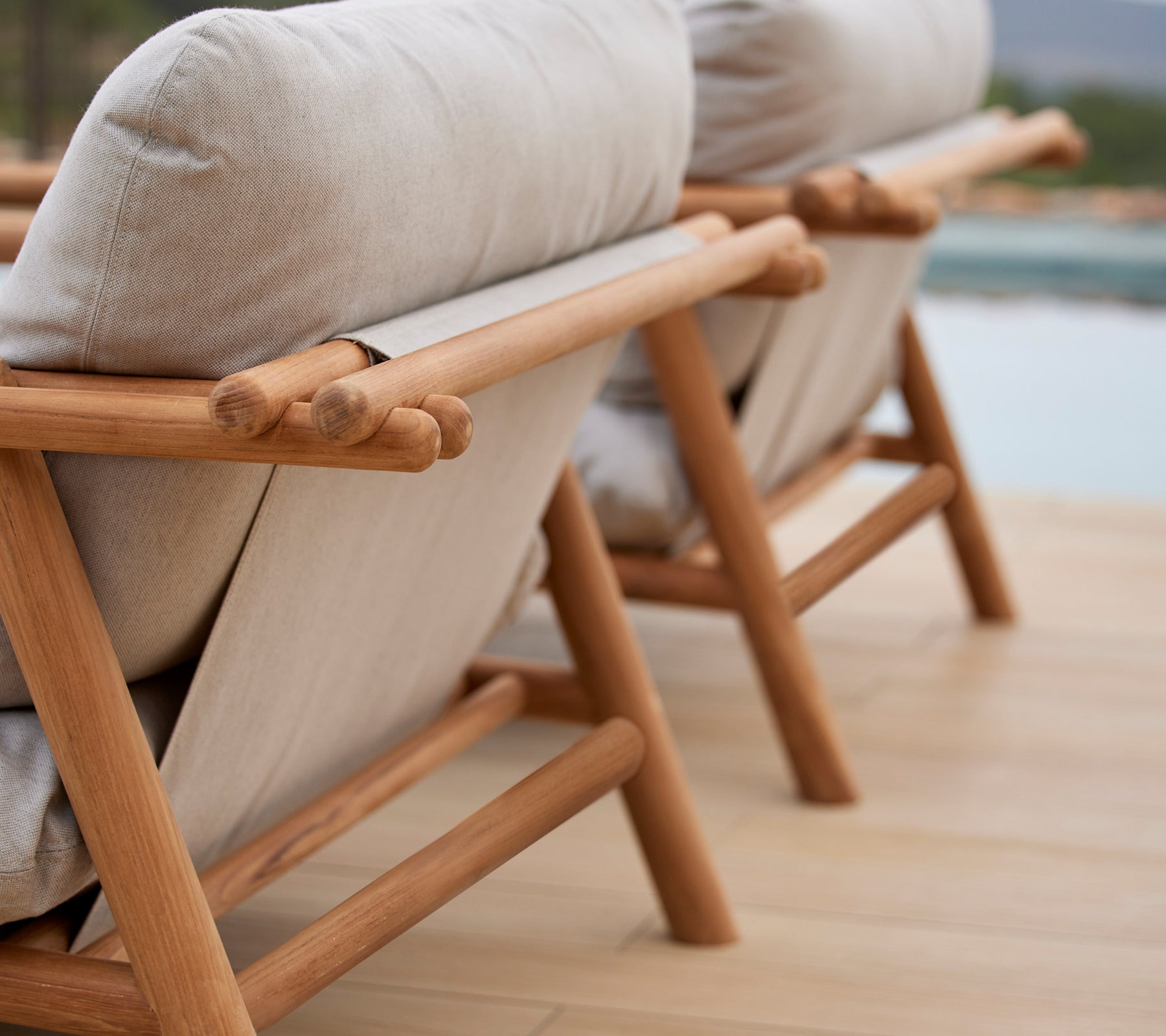 To stilige lenestoler med teakrammer og komfortable beige puter, som viser et unikt pinne-design på ryggstøtten.