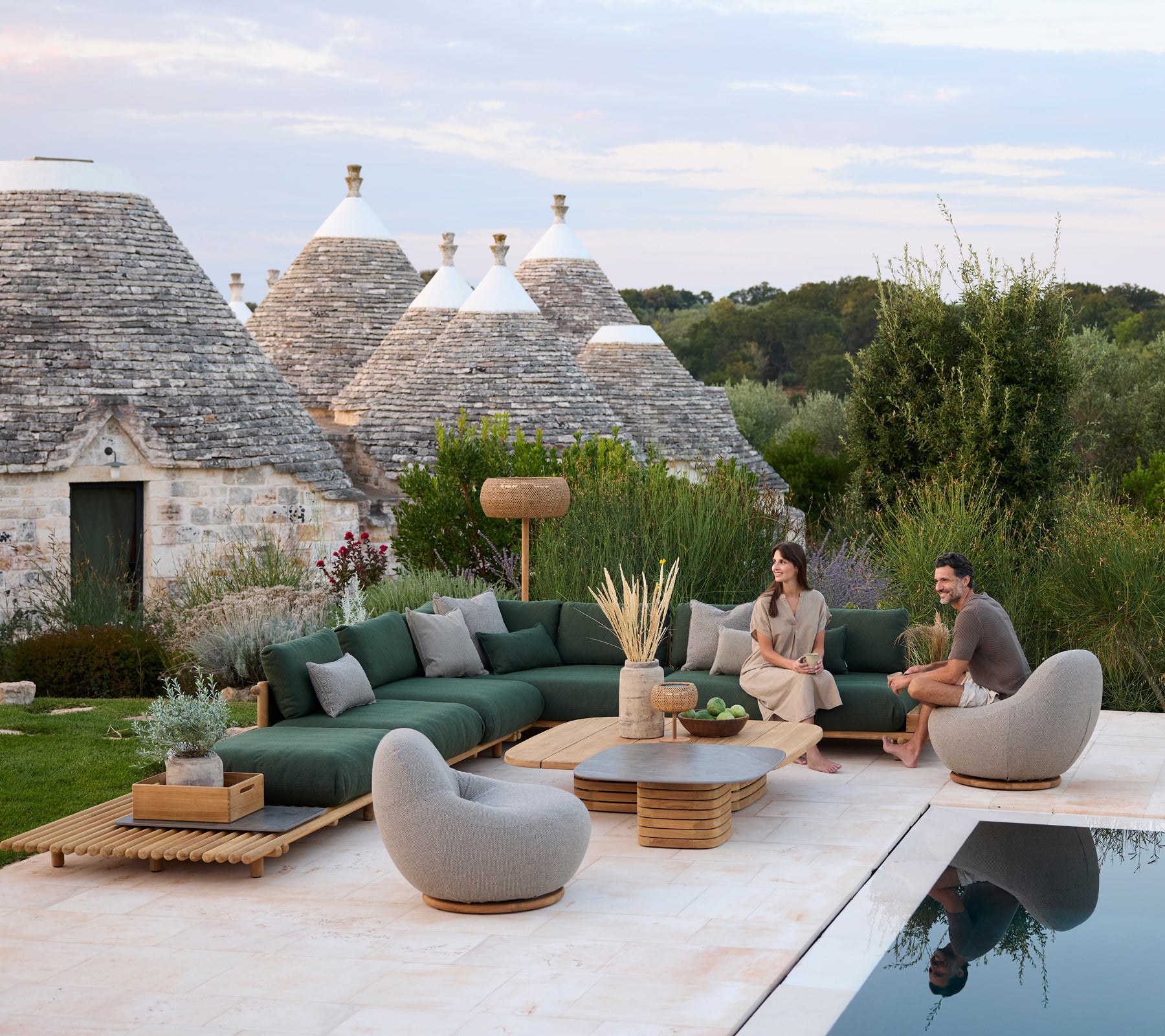 Moderne utendørs loungeområde med grønn seksjonssofa og grå stoler ved et svømmebasseng.