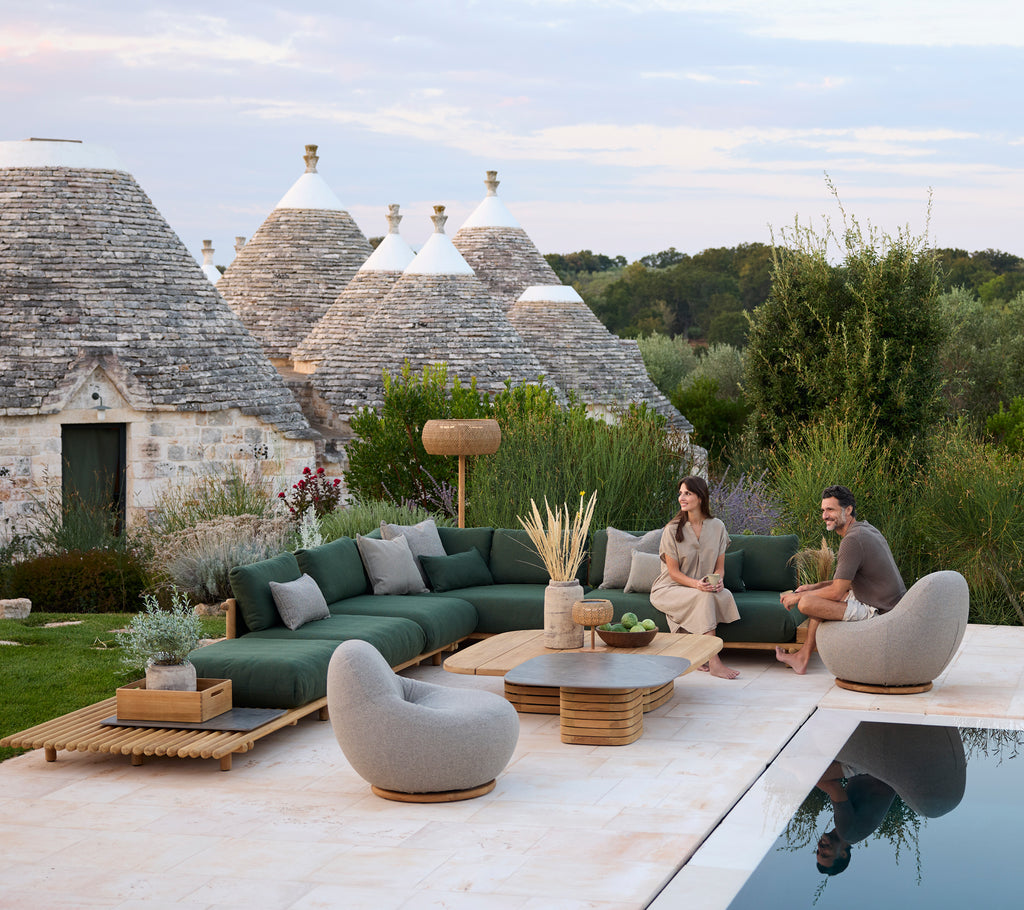 Moderne utendørs loungeområde med grønn seksjonssofa og grå stoler ved et svømmebasseng.