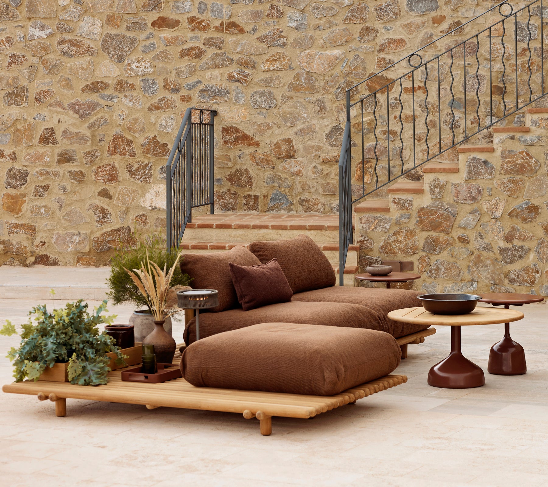 Teak lounge with plush cushions and a Glaze coffee table, complemented by decorative plants and a textured stone backdrop.