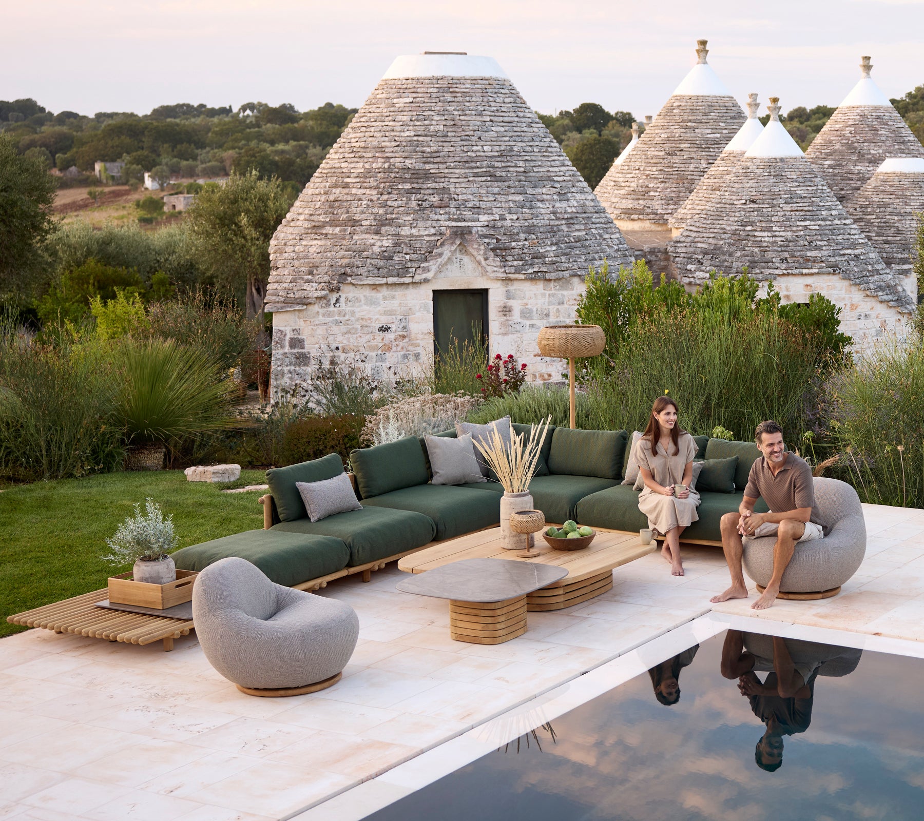 Moderne ute loungeområde med en grønn sofa, grå stol og rundt kaffebord.