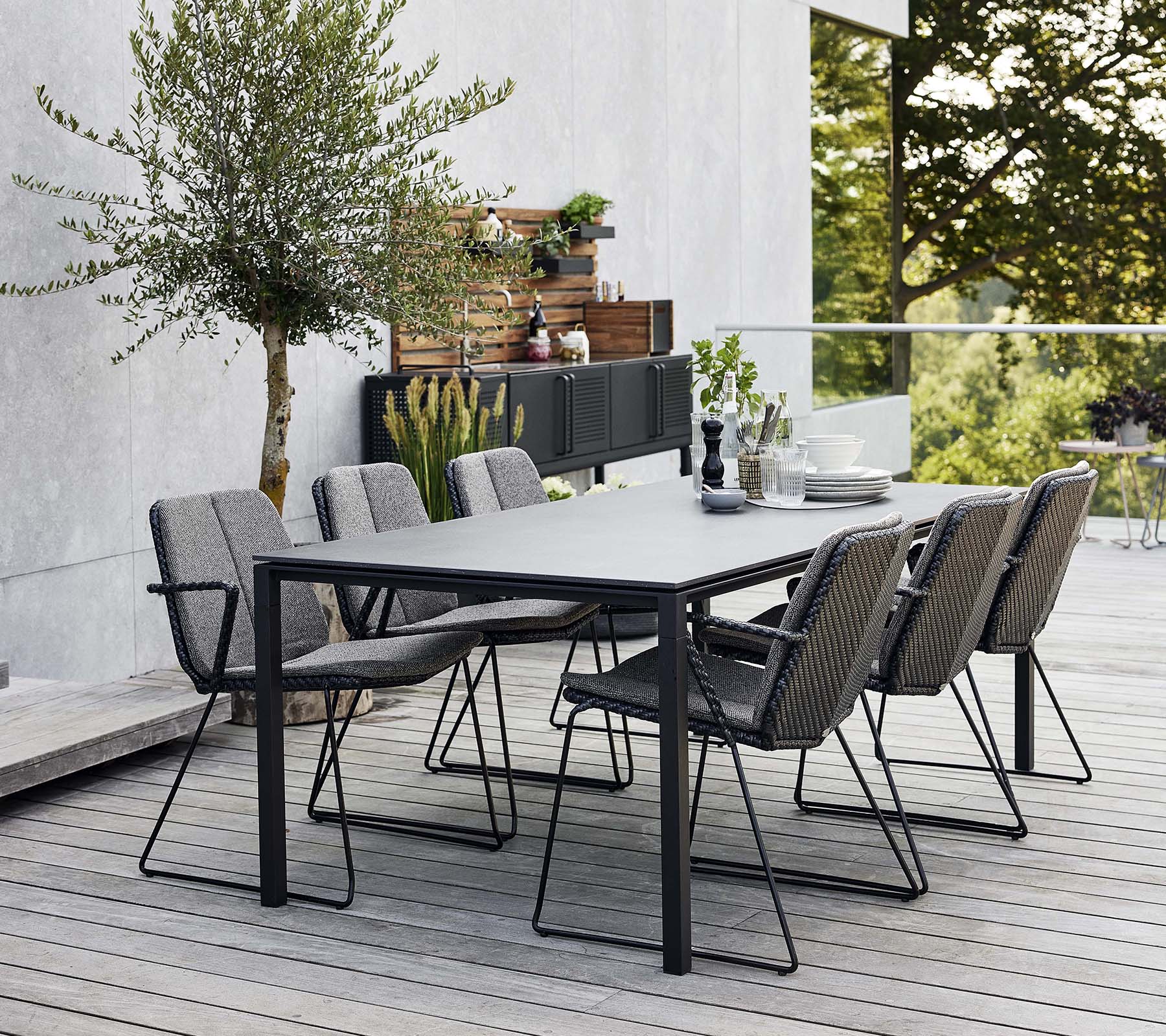 Et stilfullt ute-spisebord satt med et elegant bord og flere komfortable lenestoler, omgitt av grønt og en moderne bakgrunn.