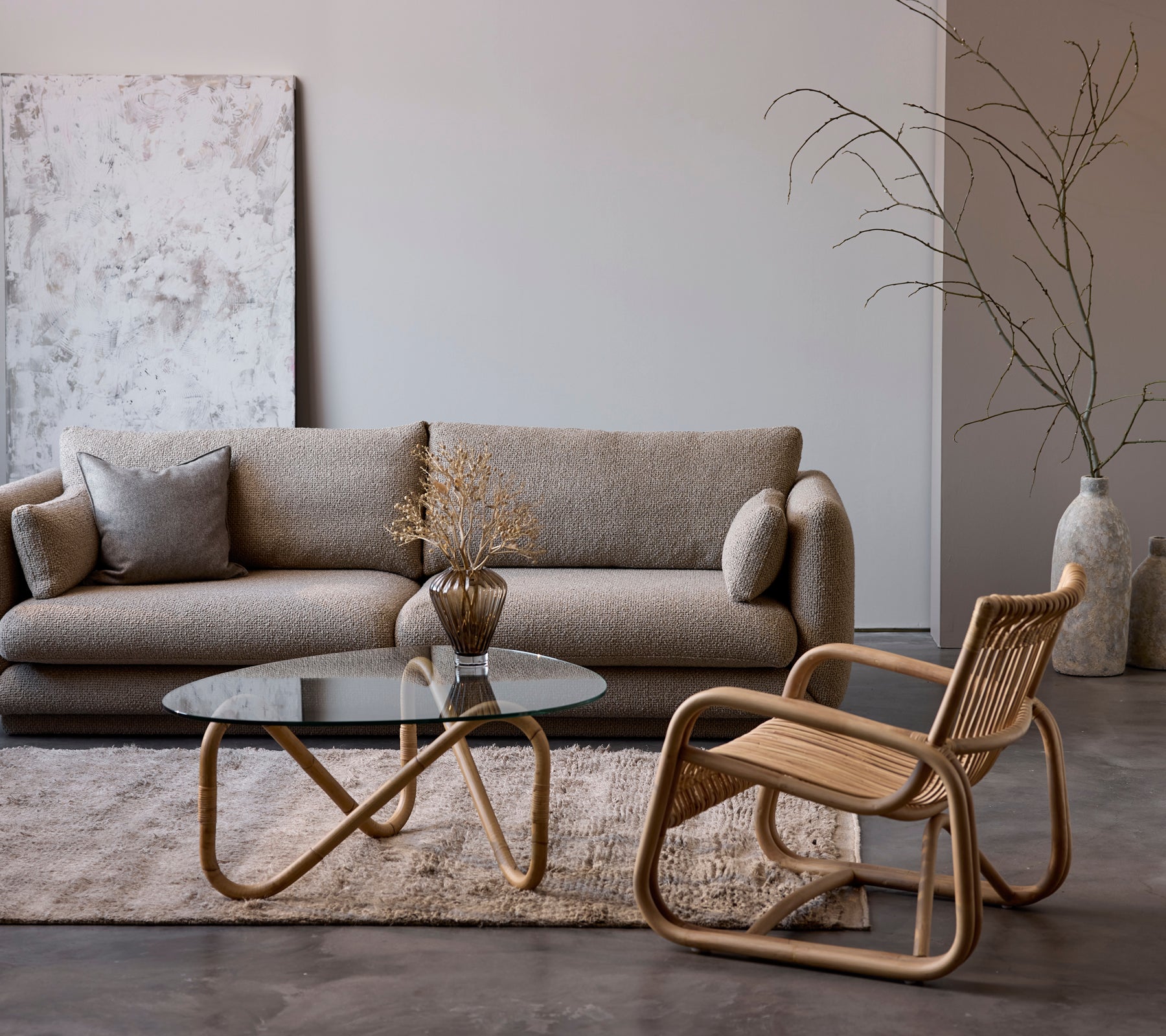 Moderne stueoppsett med en beige sofa, glassbord og vevd stol.