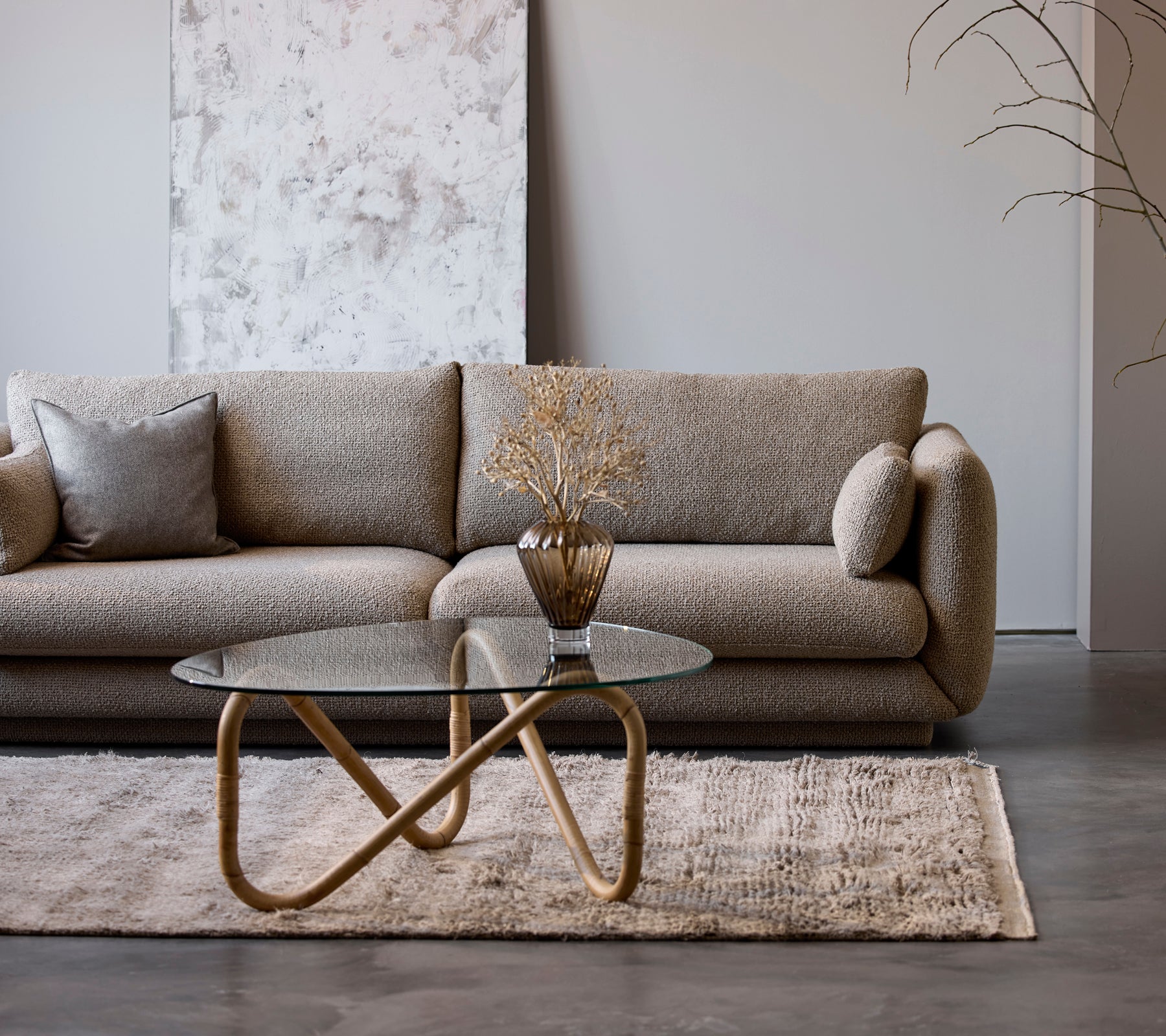 En moderne beige sofa med et glasskaffebord og en dekorativ vase i en minimalistisk loungestil.