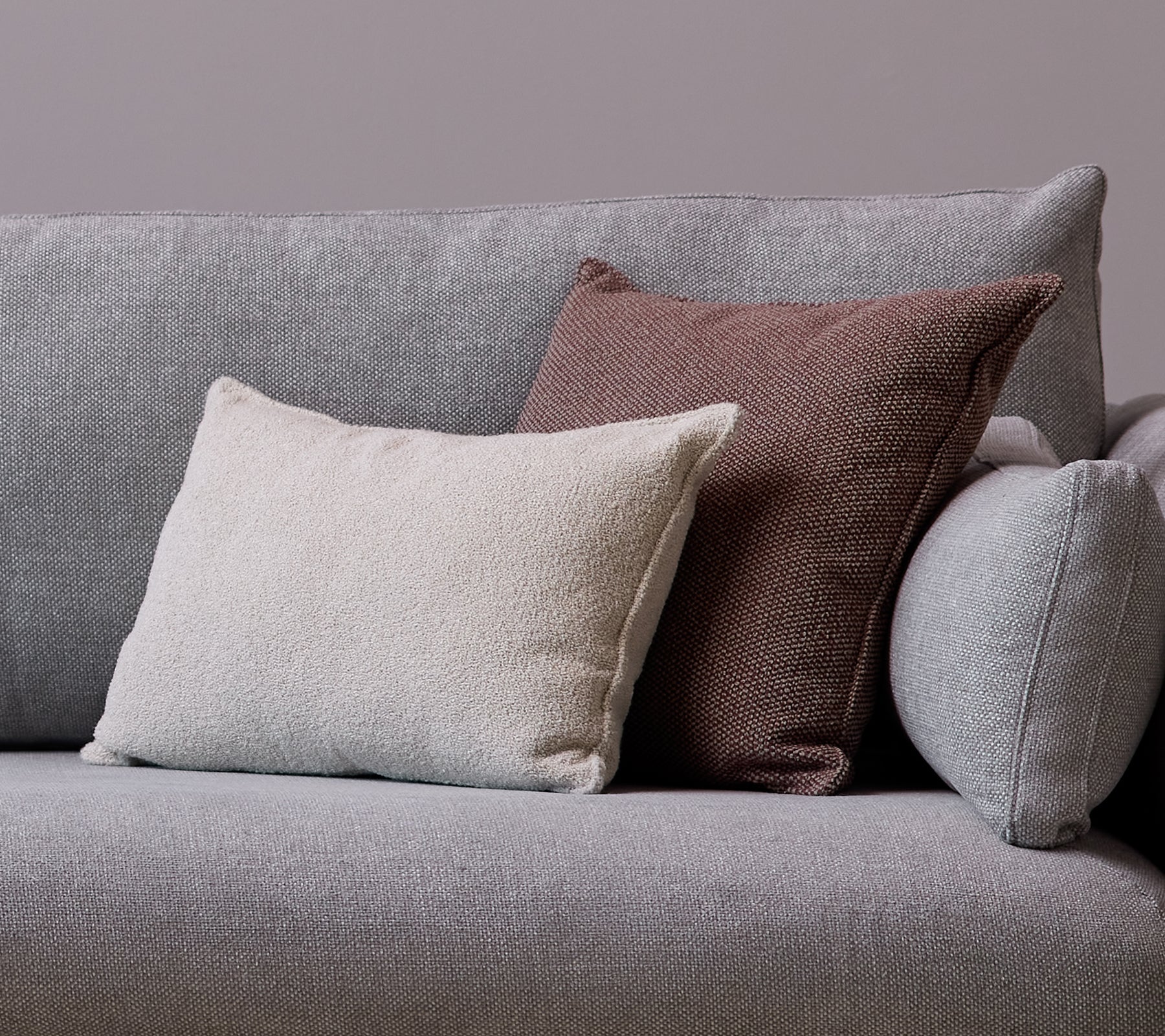 En hvit Scent scatterpute og en Wove mørk bordeaux pute er plassert på en grå sofa.