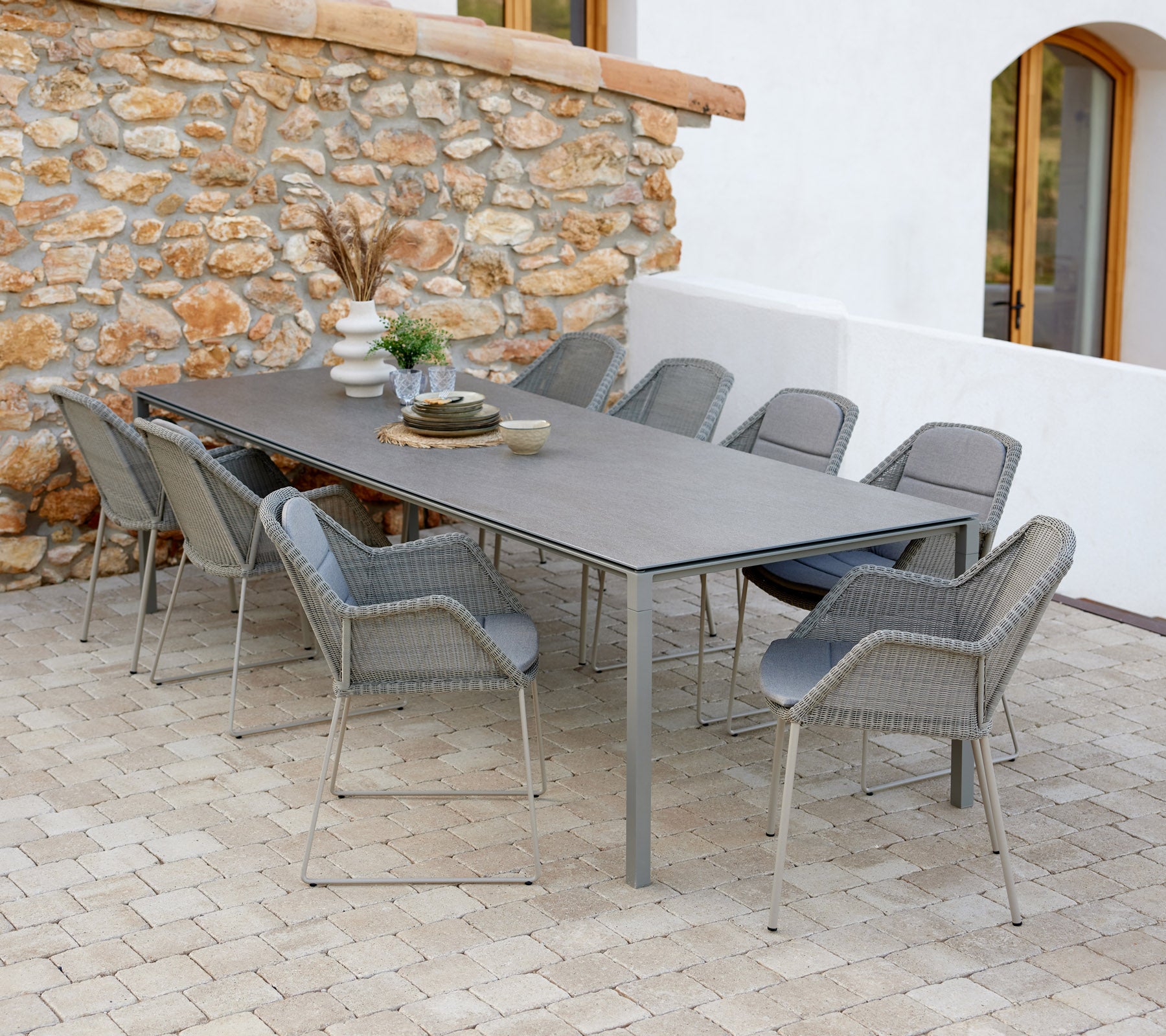 Moderne spisebord med taupe stoler, satt med dekorative gjenstander og et snev av grønt mot en steinvegg.