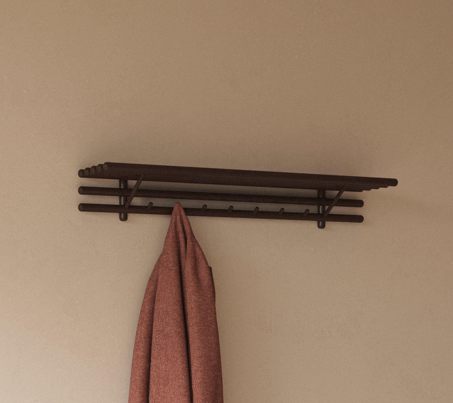 En minimalistisk hylle med flere kroker som holder et hengende klut, designet for praktisk lagring og organisering.