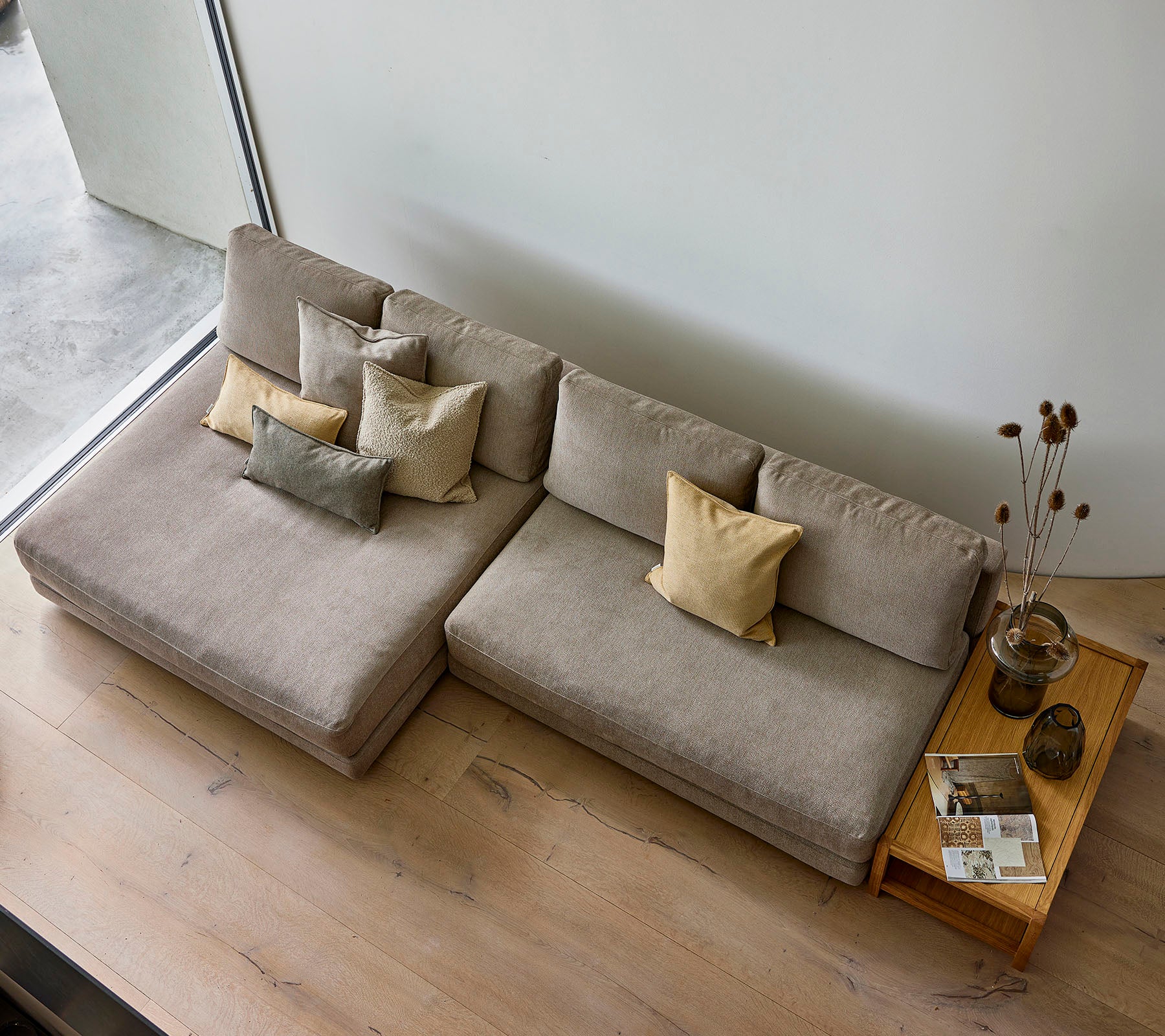 En stilfull sofa i en nøytral tone, dekorert med ulike pynteputer, ledsaget av et trebord med bøker og en vase.